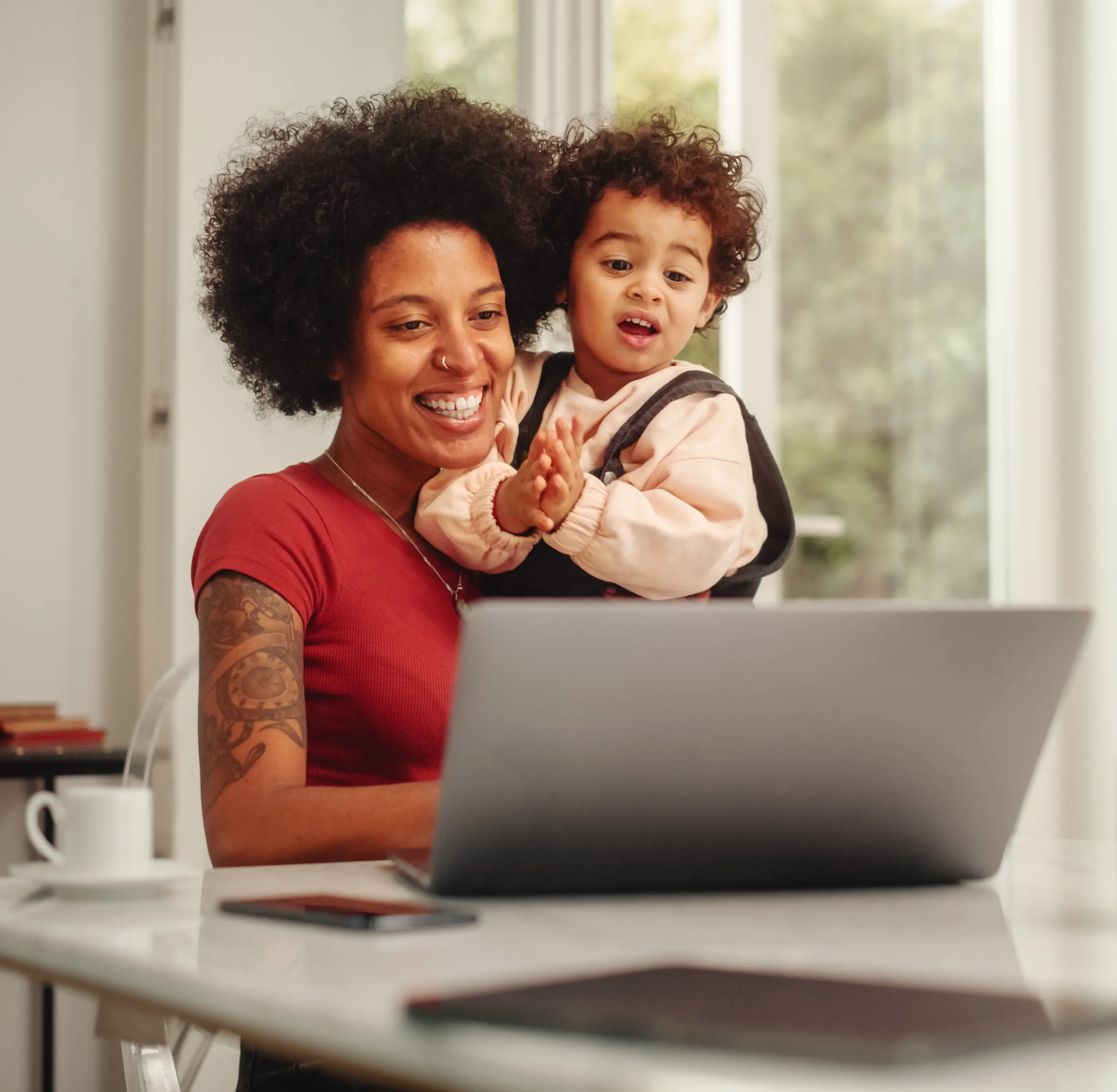 Woman holding her child while surfing the web on her laptop at home