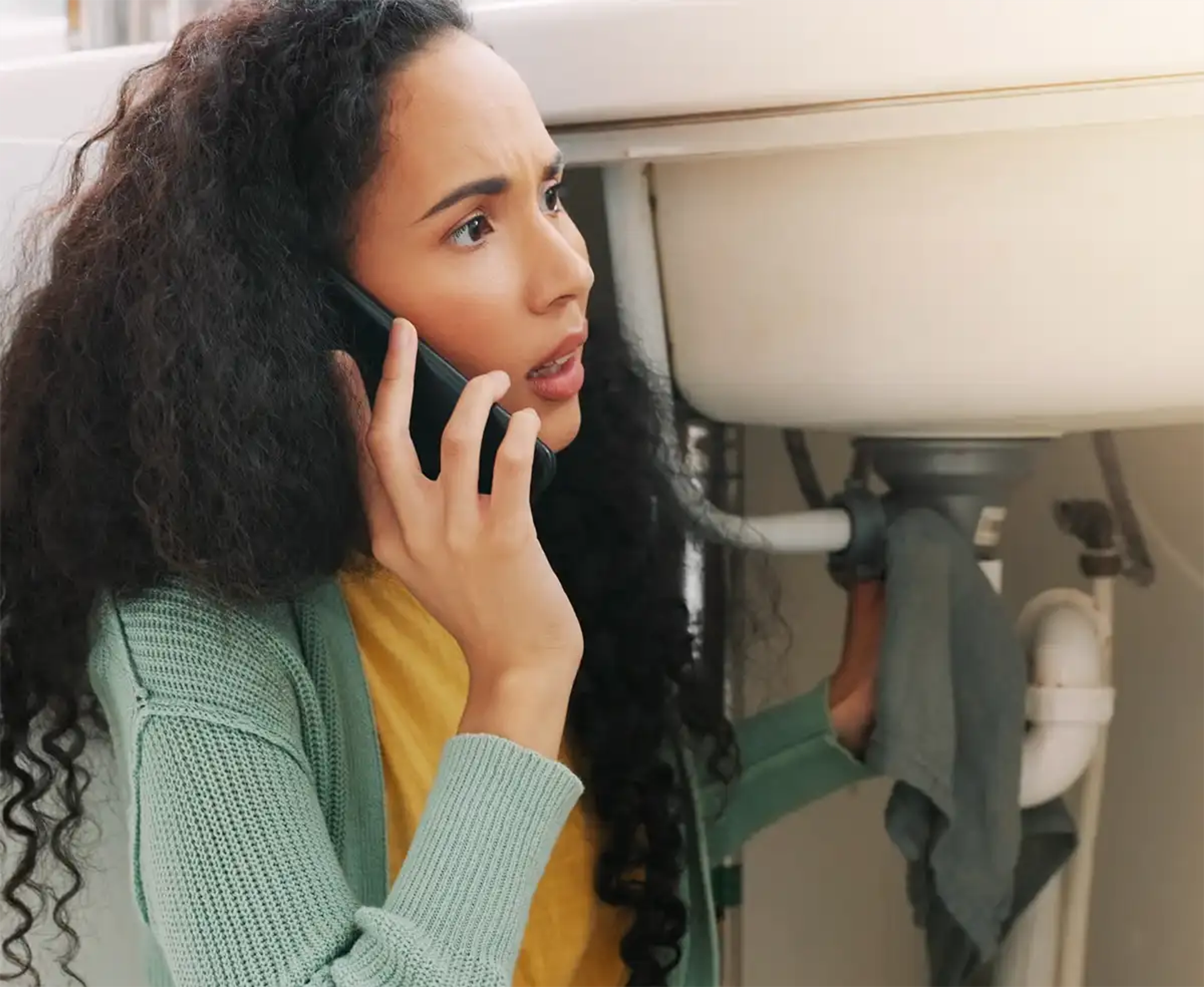 Woman on her mobile with a leaking sink