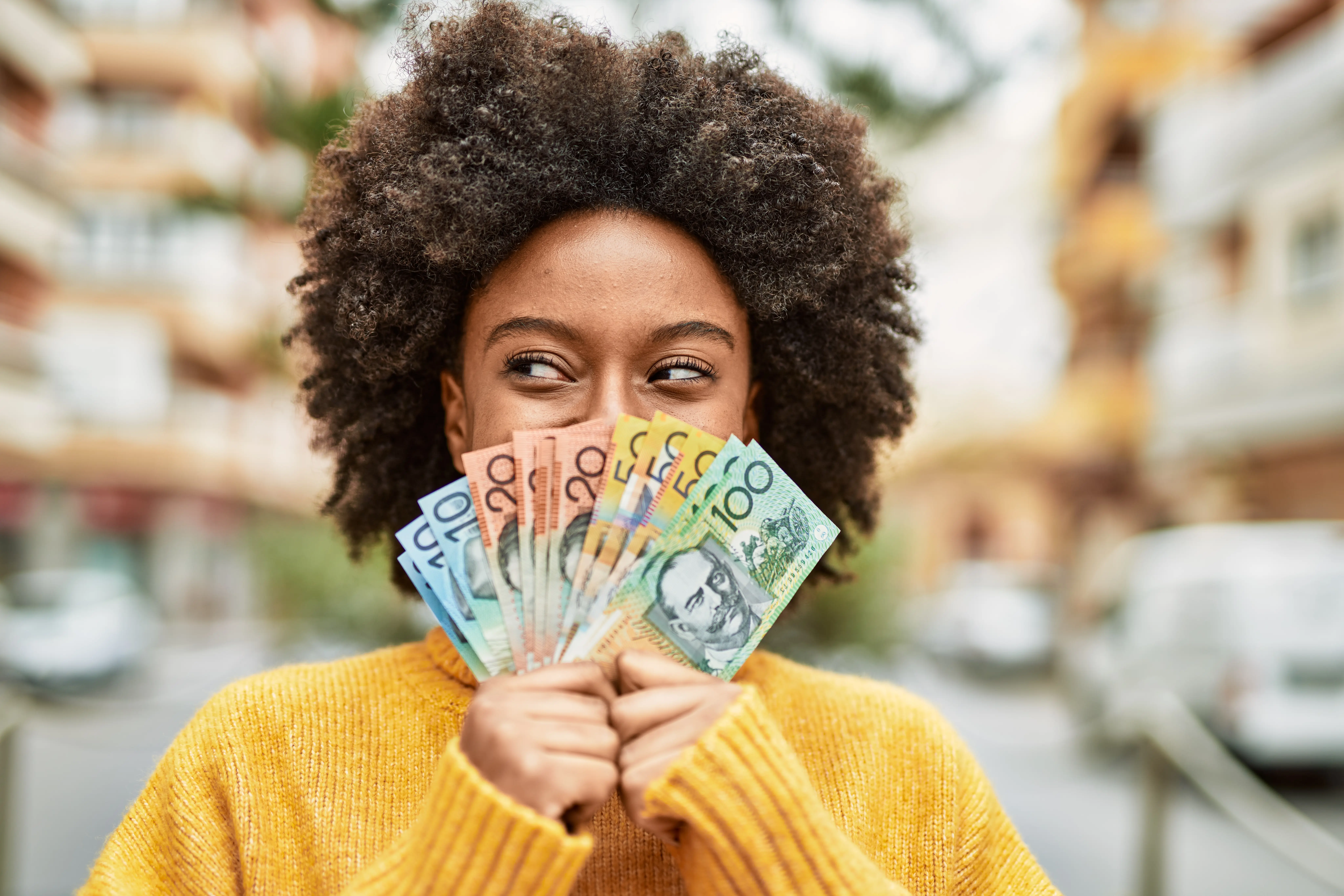 Young woman holding a fan of cash over her face with out of focus background