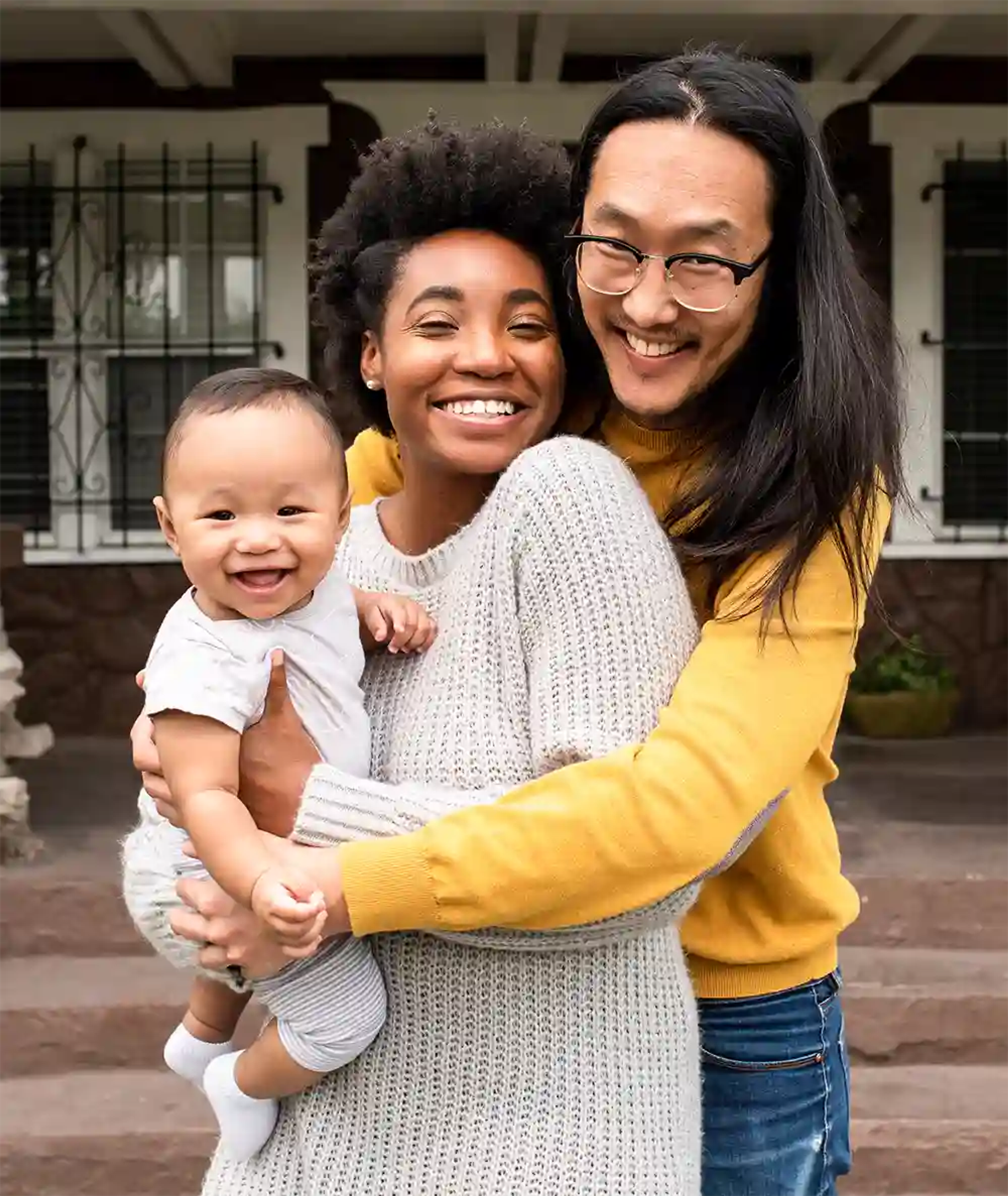 Young couple holding their baby in their arms in front of their home