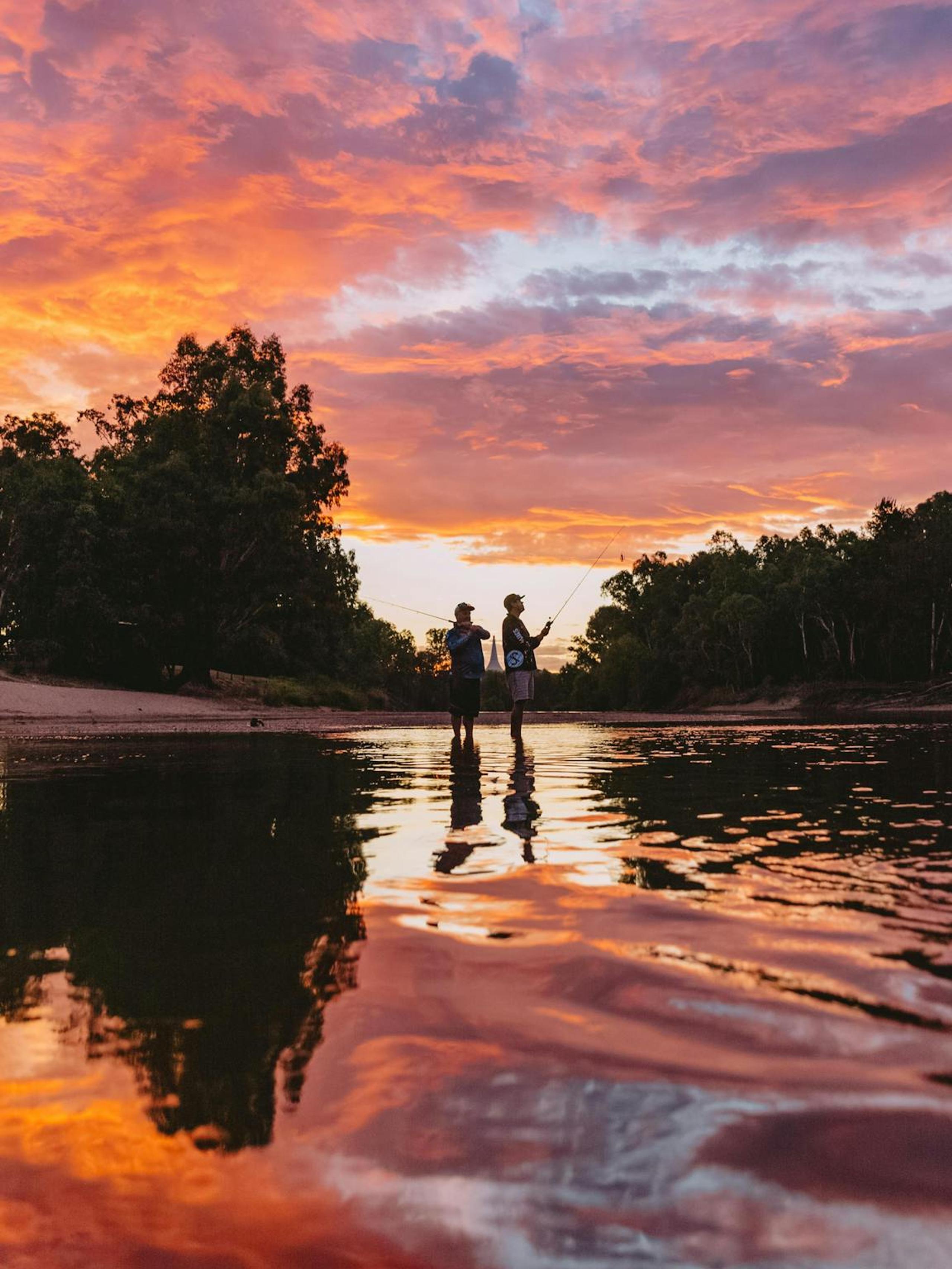 Dusk scene with two people centred and fishing with the evening sky reflected.