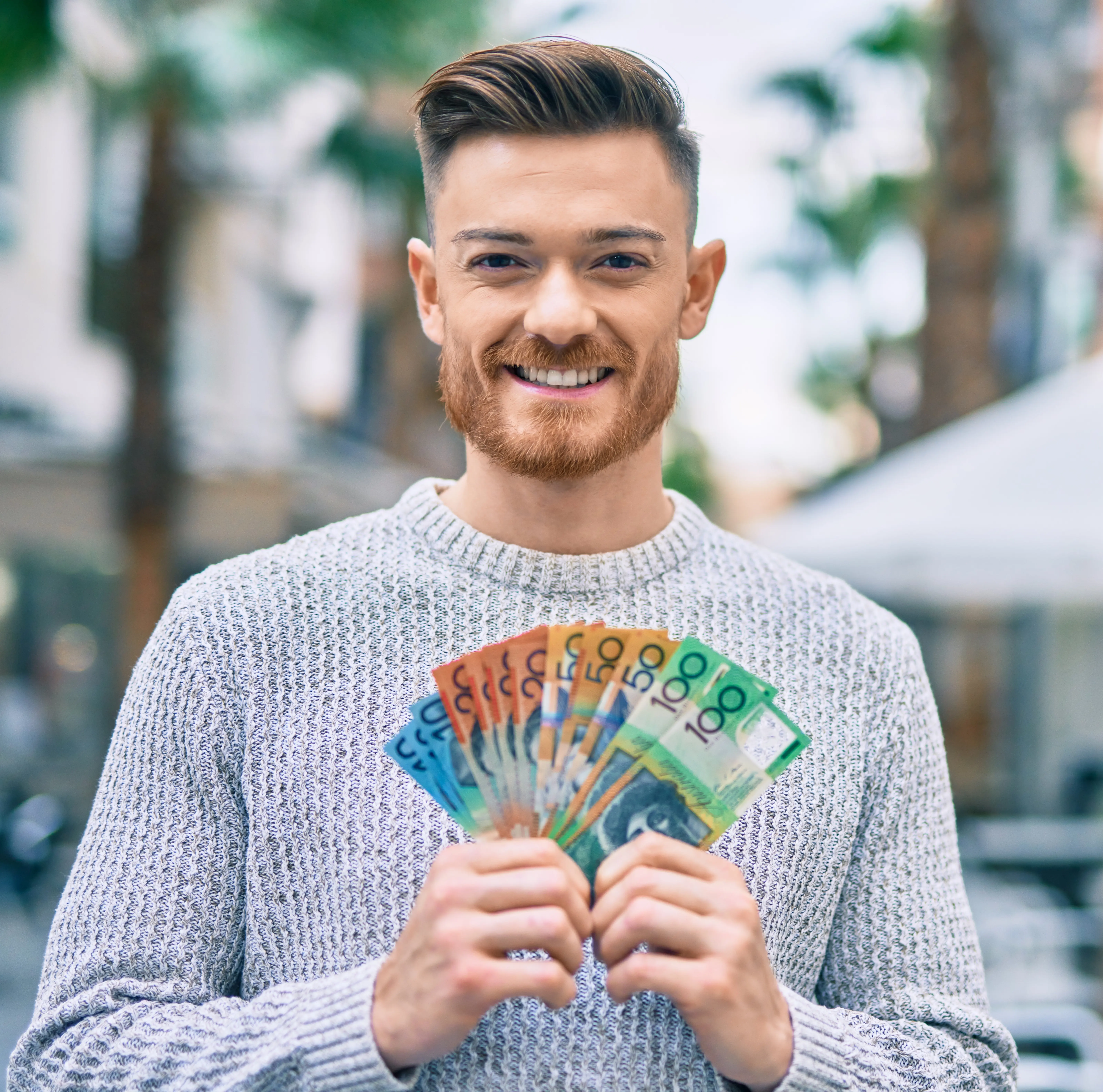 Man outside holding a fan of AUD notes in his hands