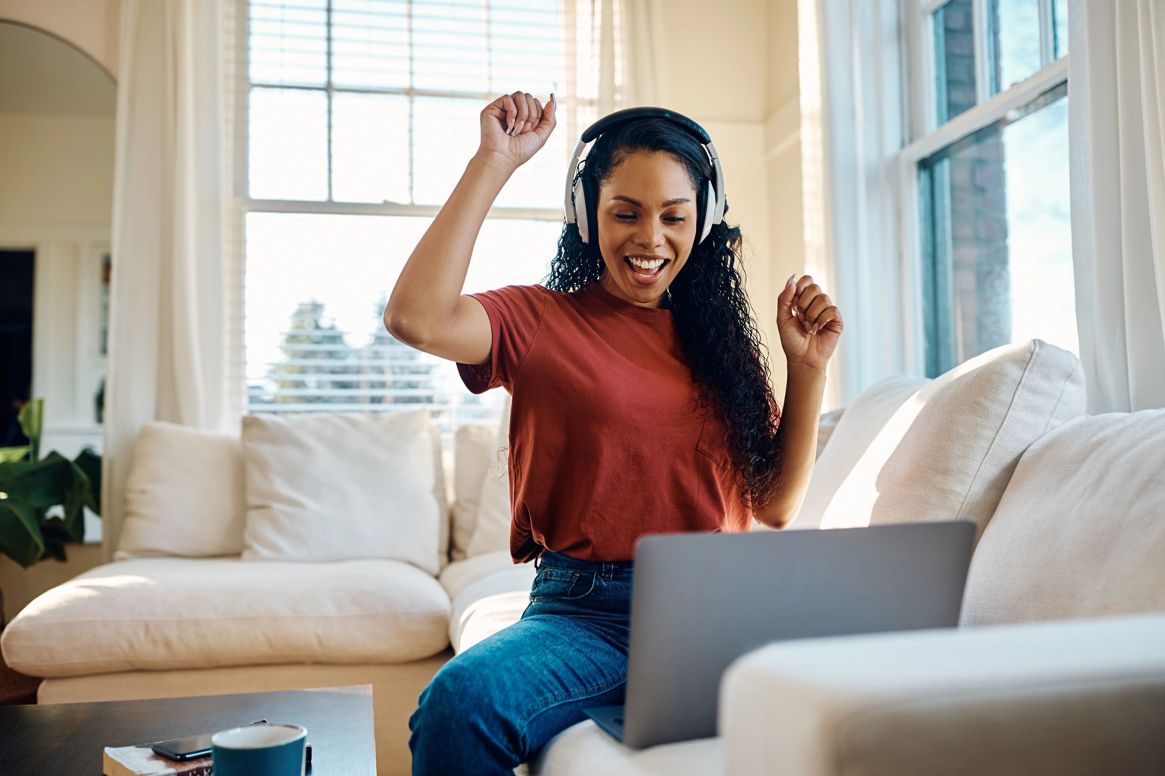 Woman at home sitting on her sofa celebrating her loan approval on her laptop screen