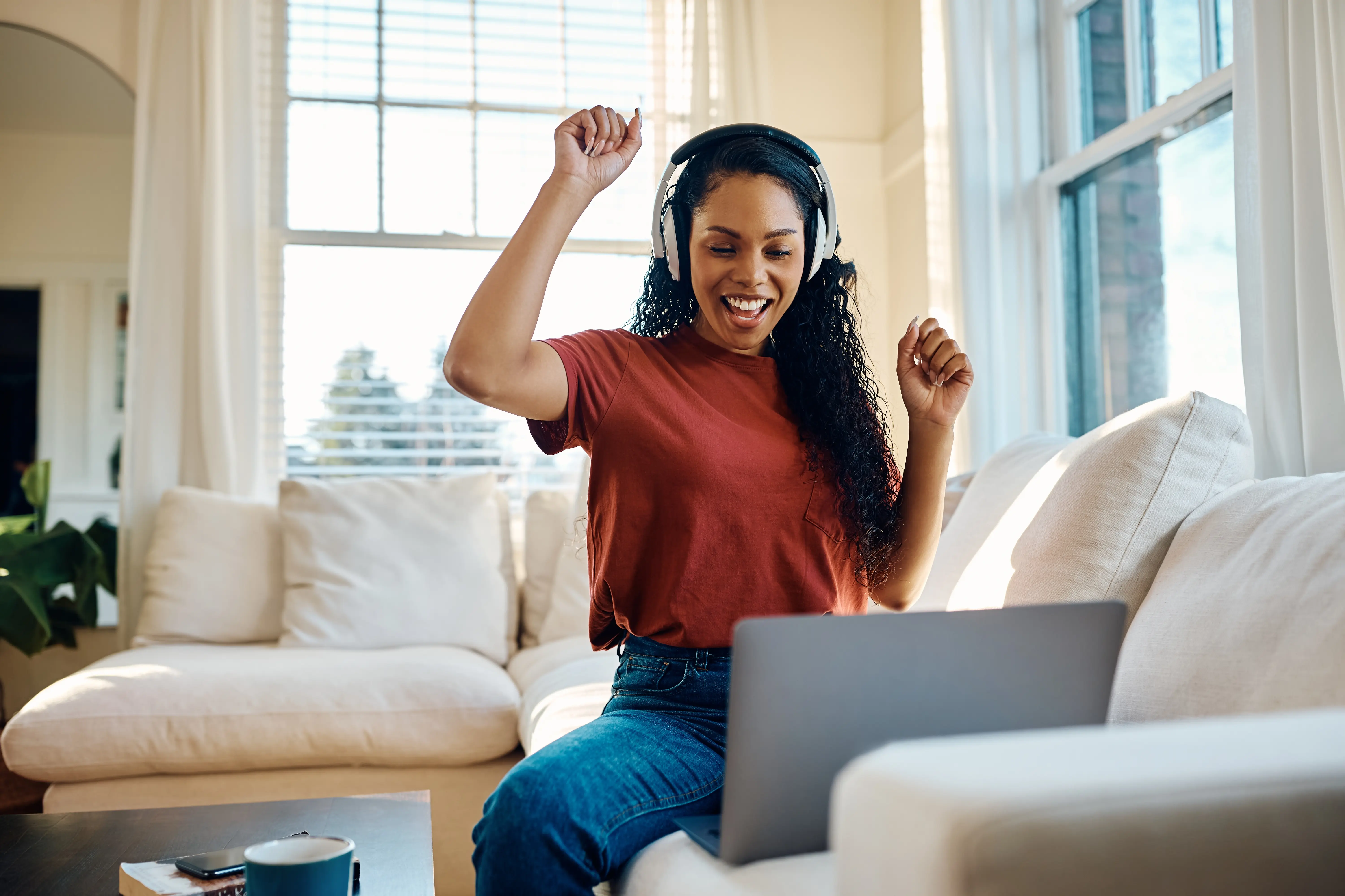 Woman at home sitting on her sofa celebrating her loan approval on her laptop screen