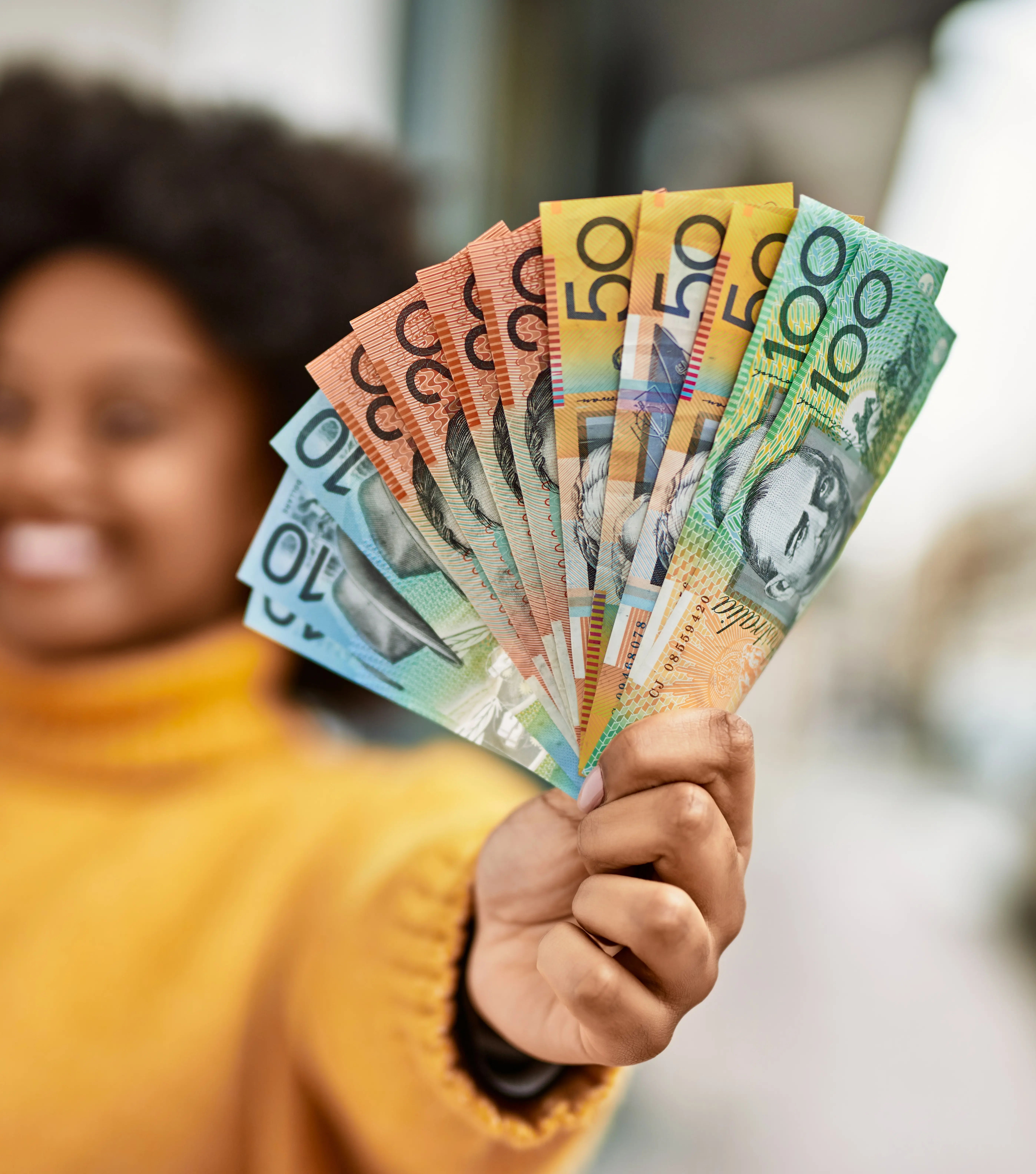 Woman in a mustard yellow sweater holds a fan of Australian cash
