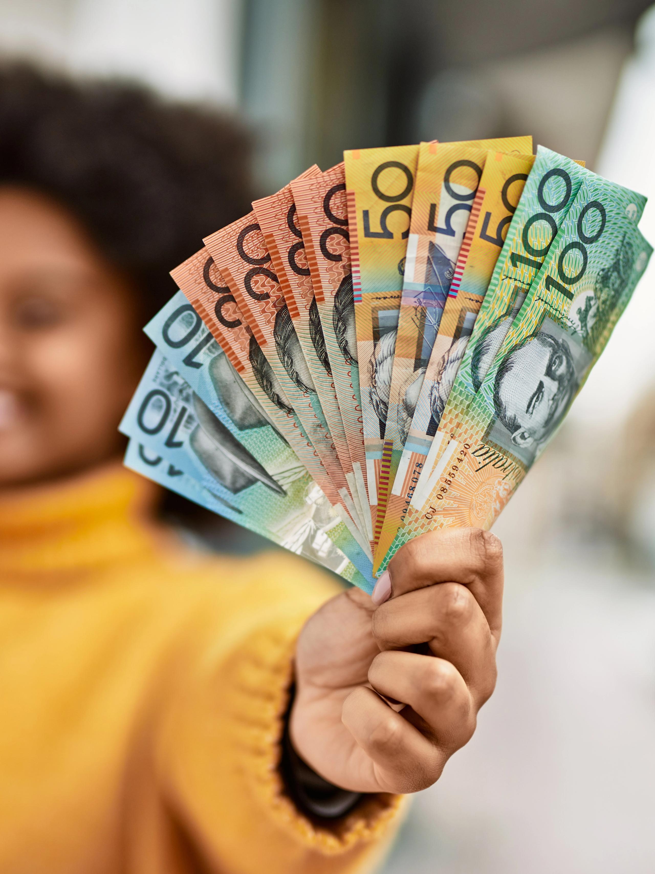 Woman in a mustard yellow sweater holds a fan of Australian cash