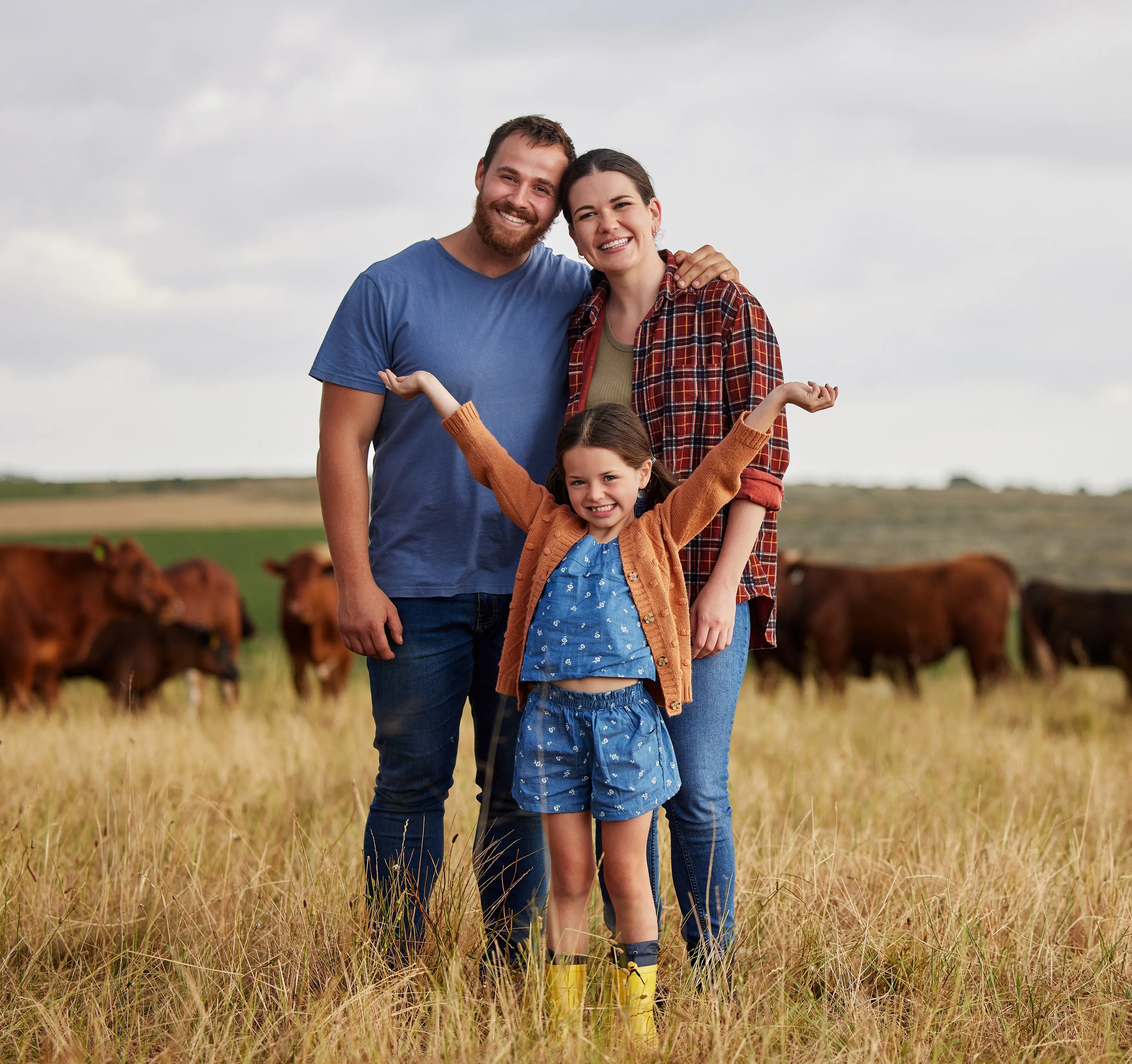 Country family standing in a field with cows all around them in the background