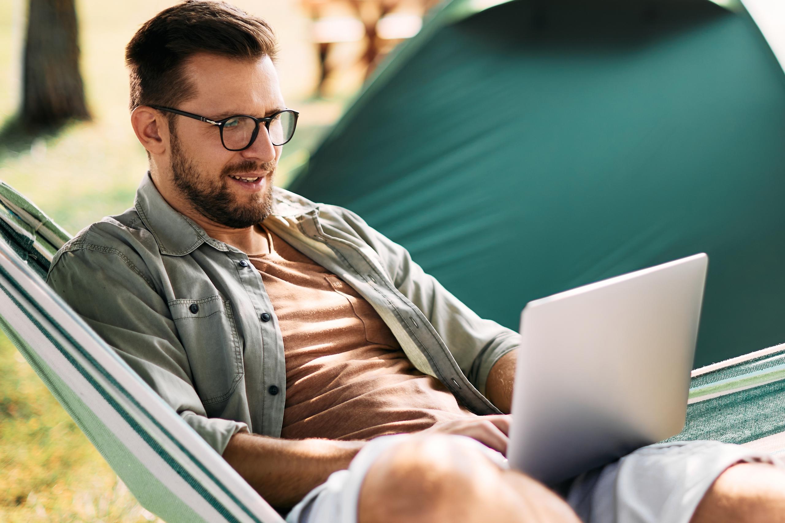 Man reclining in hammock and checking his laptop