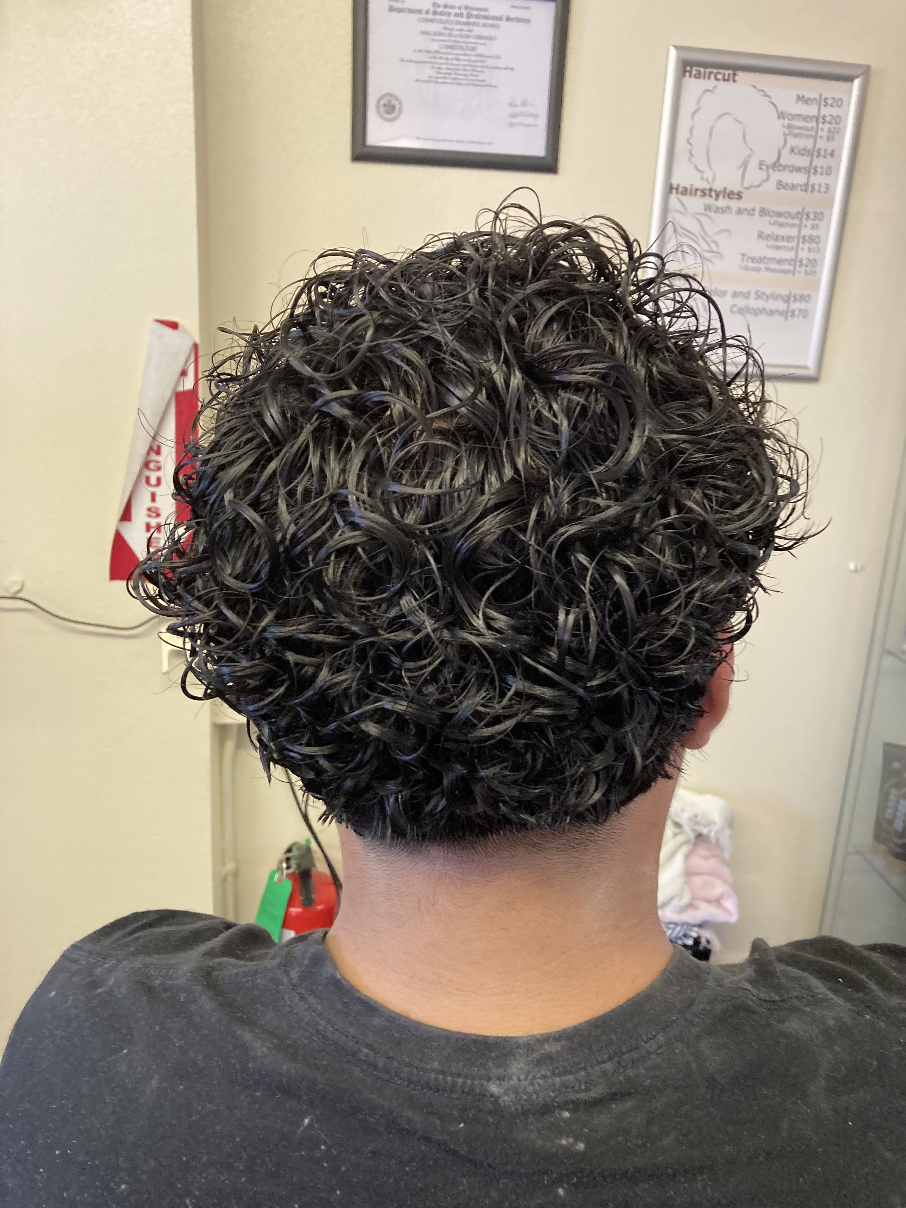 Boy with short to medium-length hair styled in tight, defined curls. The curls are uniformly distributed. The hair at the sides and back is trimmed slightly shorter, providing a subtle contrast to the fuller curls on top.