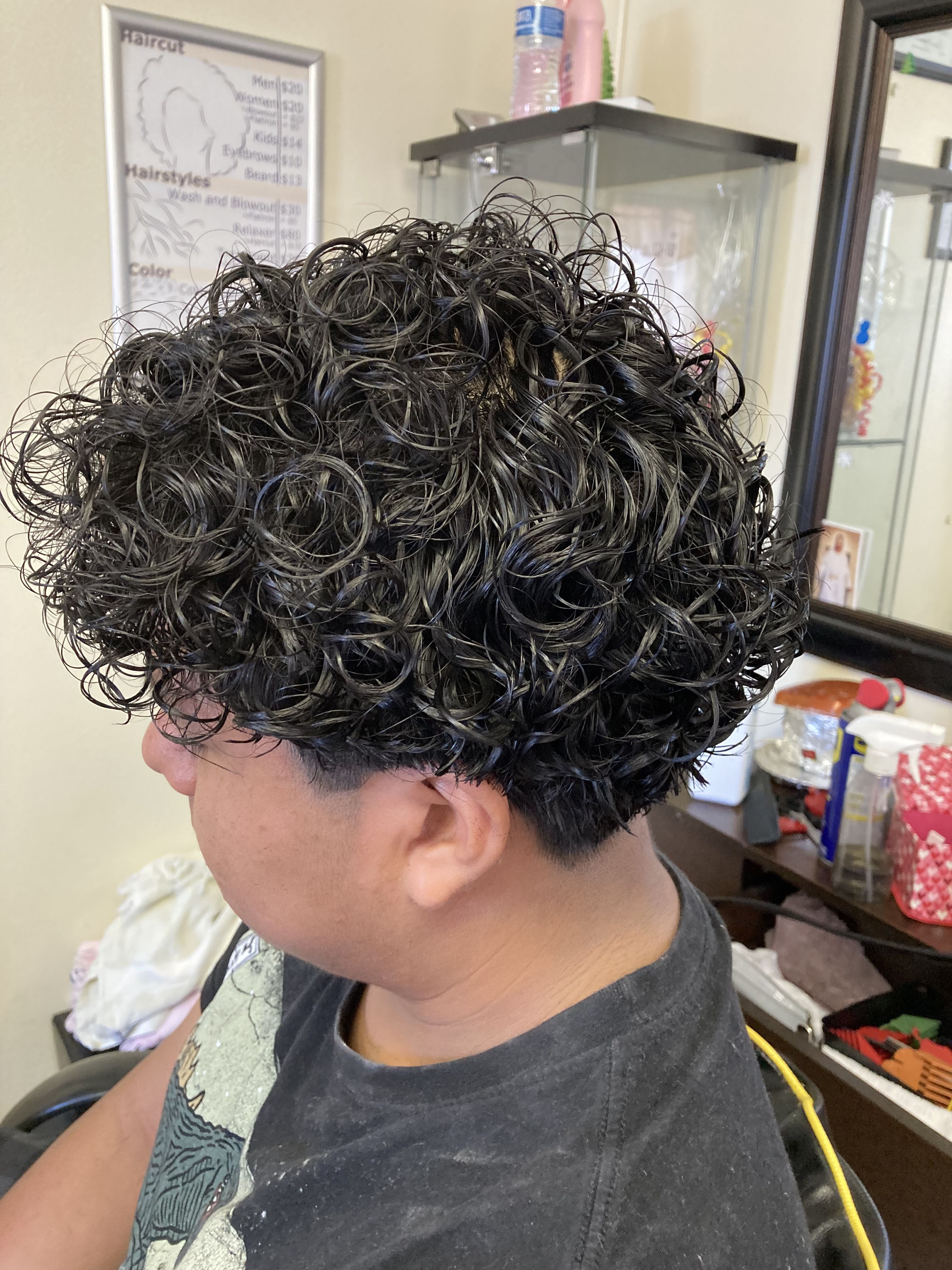 Boy with short to medium-length hair styled in tight, defined curls. The curls are uniformly distributed. The hair at the sides and back is trimmed slightly shorter, providing a subtle contrast to the fuller curls on top.