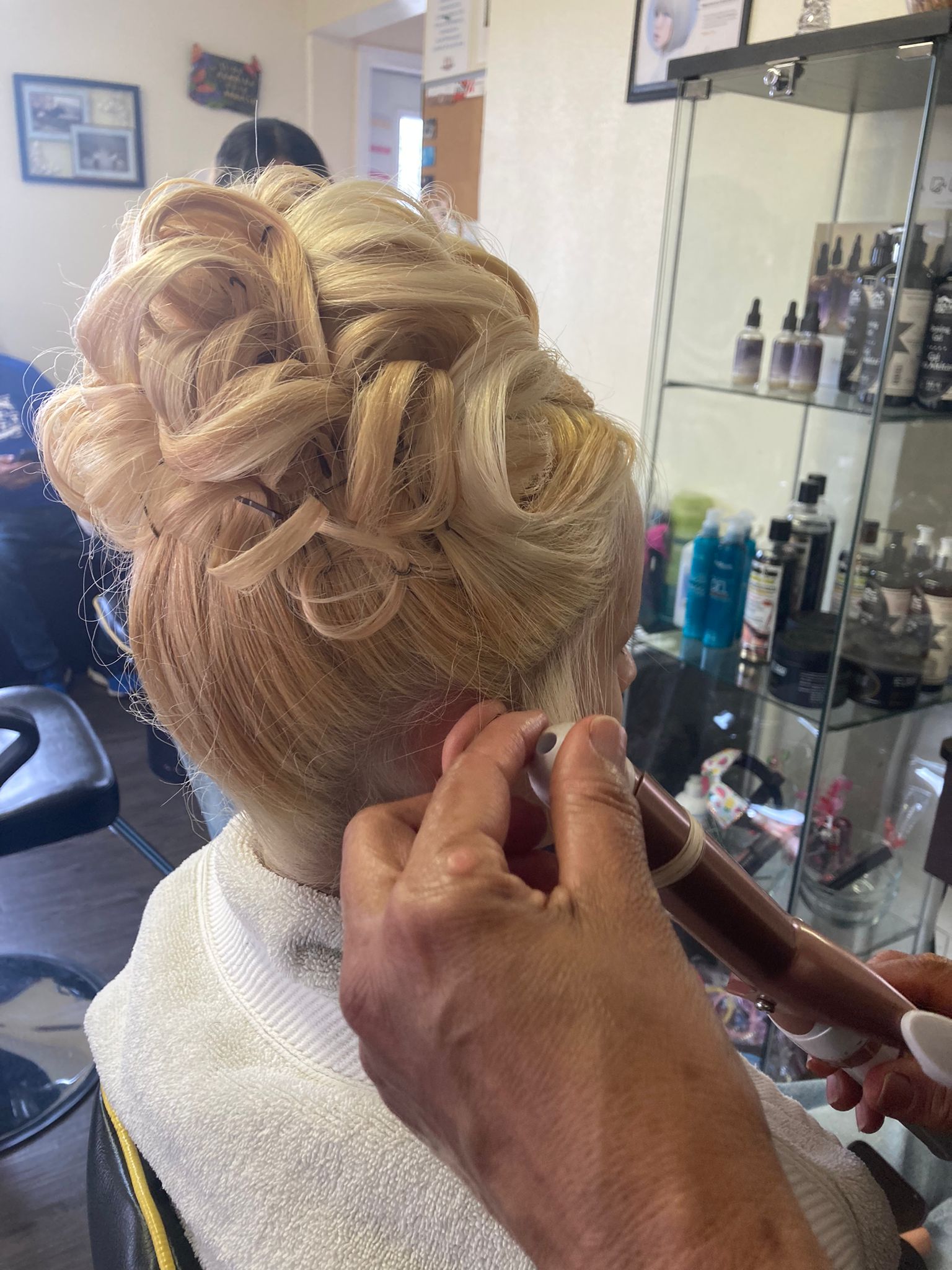 A woman with curled sections of blonde hair, intricately pinned together at the back of the head. The curls are arranged in a voluminous and elegant pattern. framed to the side.