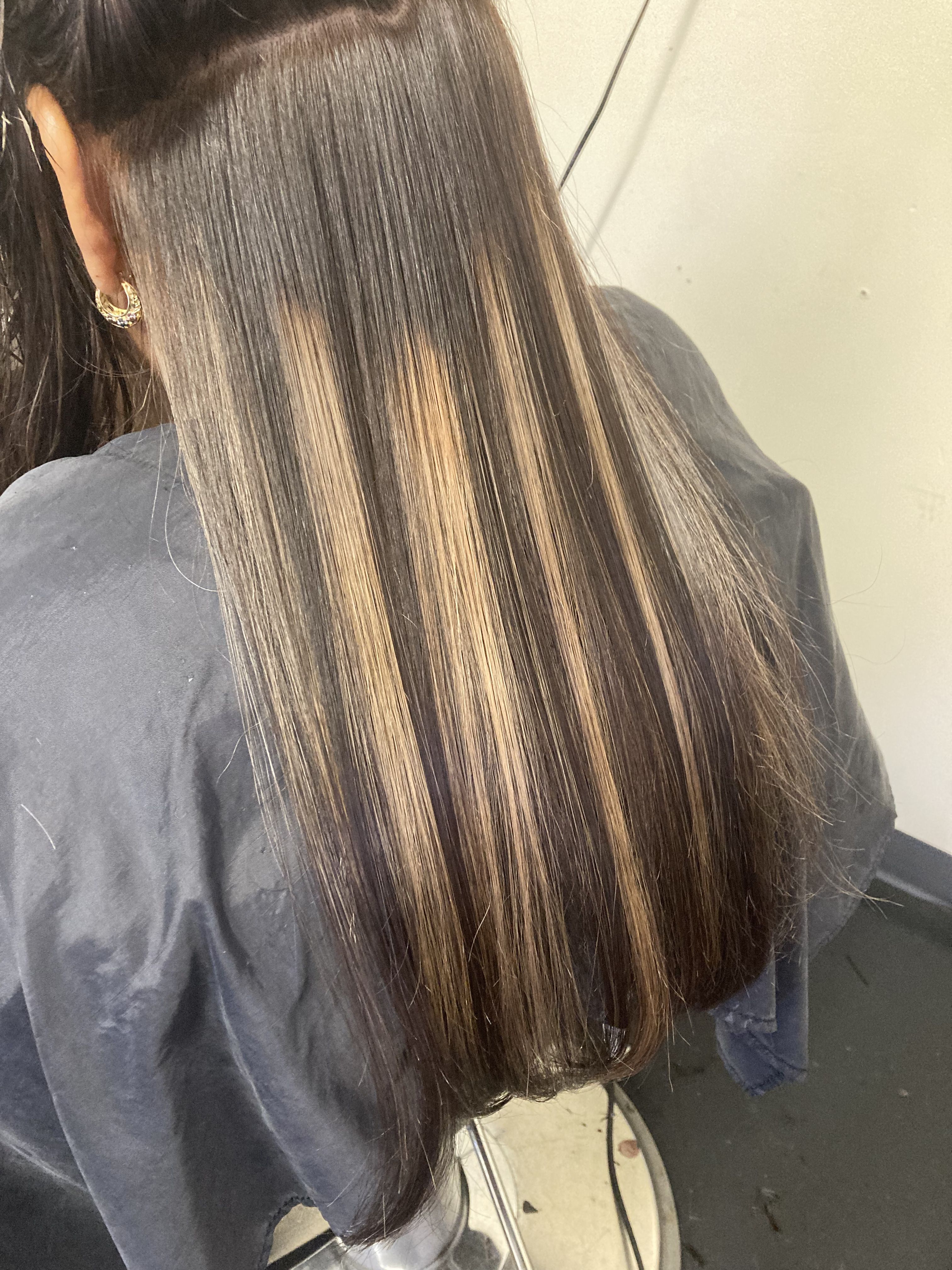 Close-up view of a person’s hair styled with long, straight, dark hair that features light highlights. The highlights are strategically placed to create a striped effect, adding contrast and dimension to the sleek hair.