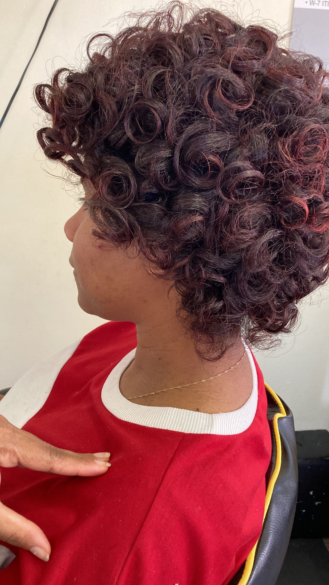 Woman with short, curly hairstyle featuring tight, voluminous ringlets throughout. The curls are uniformly coiled, creating a dense and textured appearance.