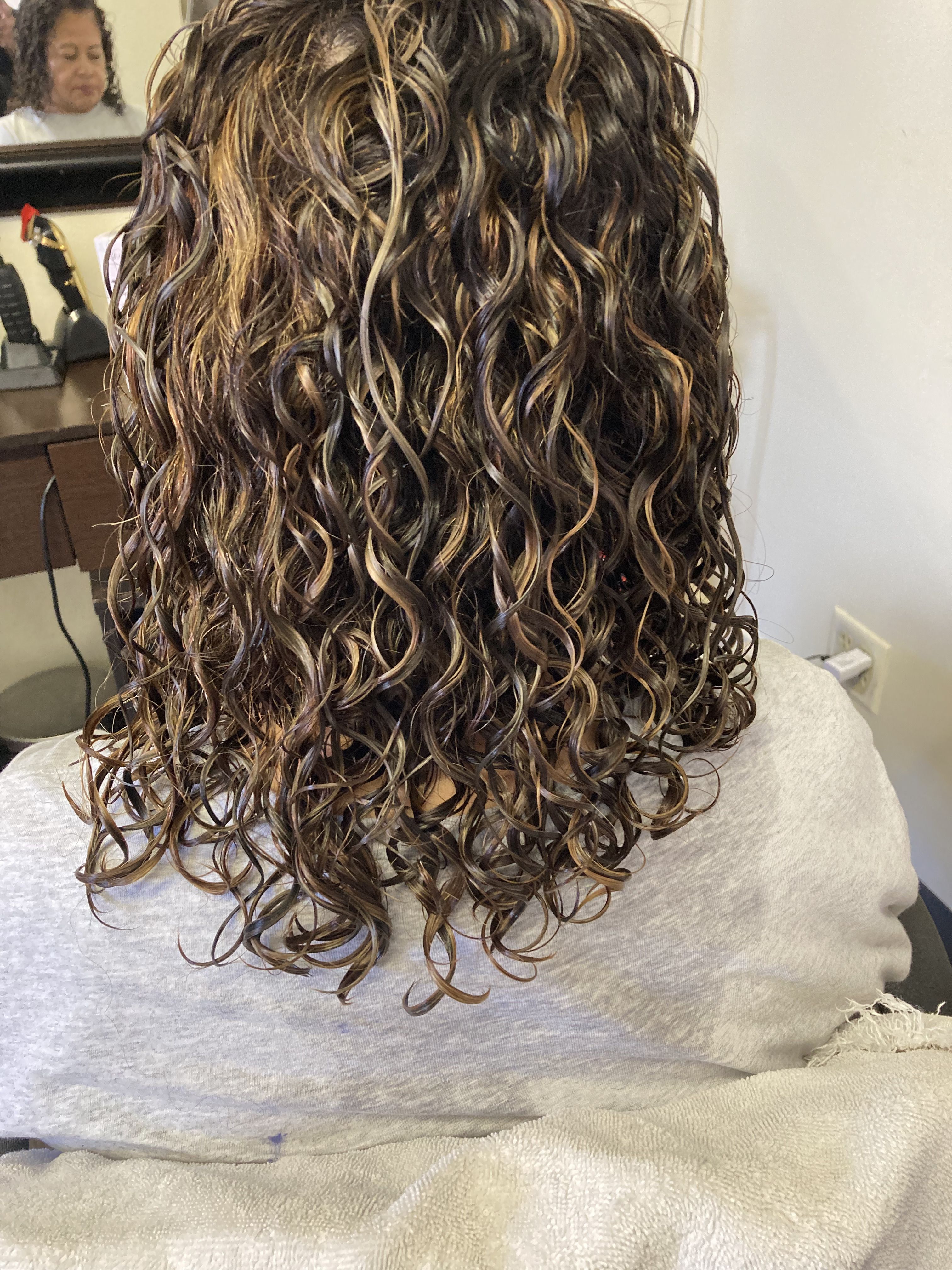 The hairstyle features medium-length, dark curly hair with golden highlights. The curls are well-defined, creating a voluminous and textured look with the highlights adding depth and dimension throughout the hair.