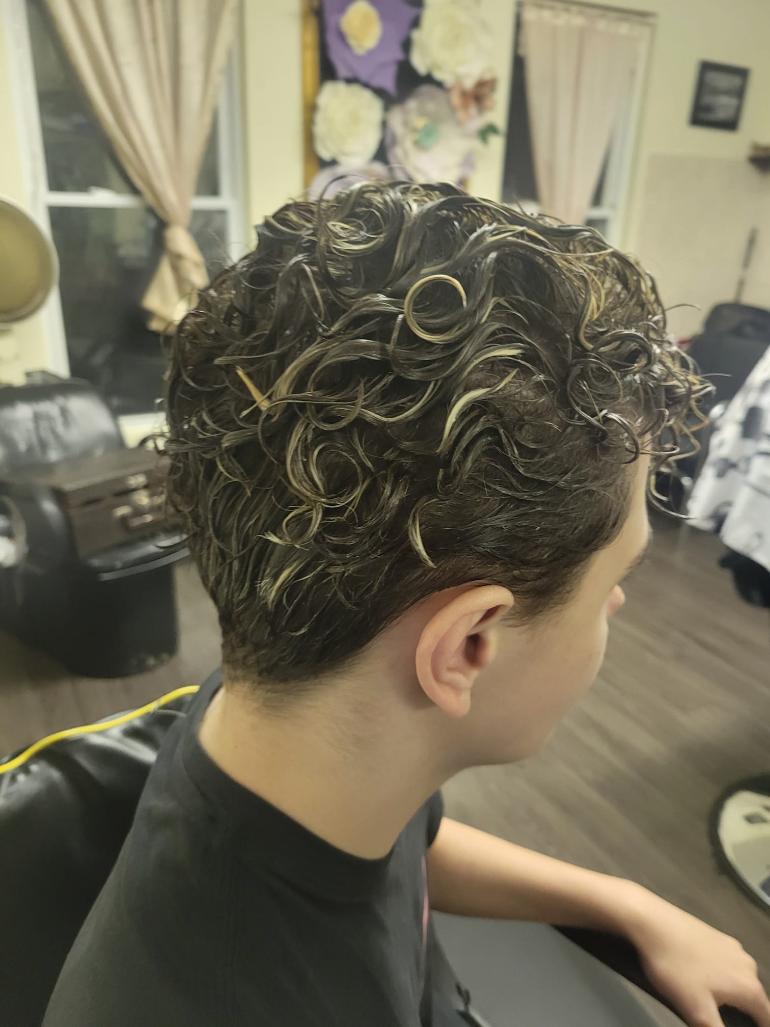 A short curly hairstyle featuring well-defined wet-look curls. The sides are tapered neatly, blending into the longer curls on the top. The style is clean and polished