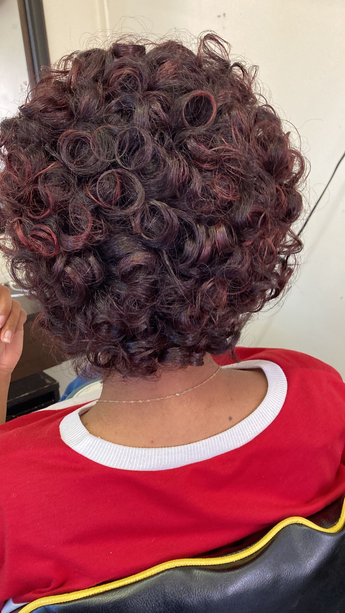Woman with short, curly hairstyle featuring tight, voluminous ringlets throughout. The curls are uniformly coiled, creating a dense and textured appearance.