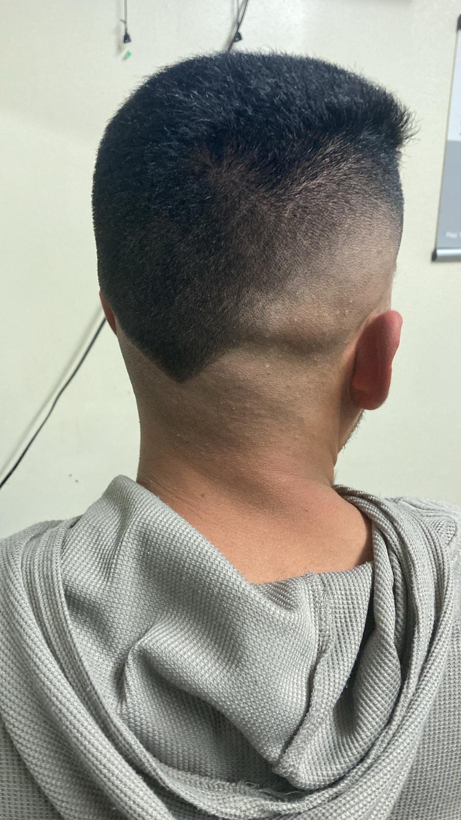 A sharp, modern haircut featuring a high fade on the sides and back, blending seamlessly into slightly longer hair on top. The nape area has a distinct V-shaped design for a bold, clean finish.