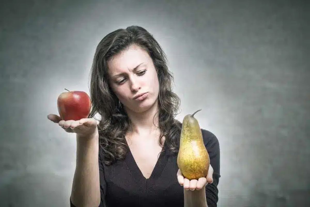 Frau wägt das Gewicht ab von einer Birne und einem Apfel. welche sie in jeweils einer Hand hält