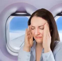 Frau sitzt im Flugzeugsitz und hält sich gestresst die Schläfen