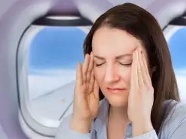 Frau sitzt im Flugzeugsitz und hält sich gestresst die Schläfen
