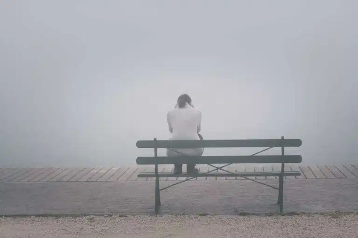 eine Person sitzt mit dem Rücken zum Betrachter im Nebel auf einer Bank