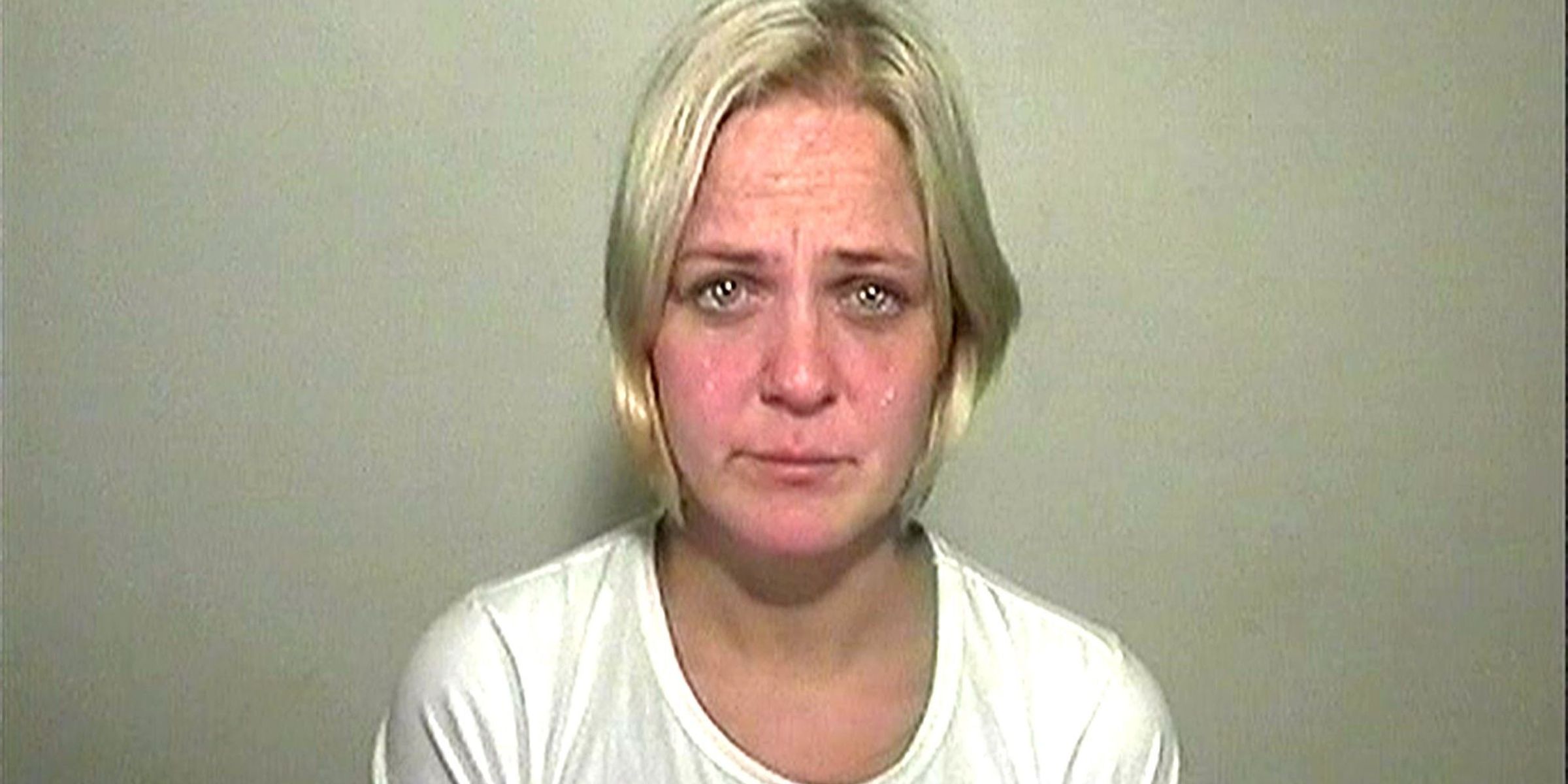 A woman in a white t-shirt looks directly into the camera with teary eyes.