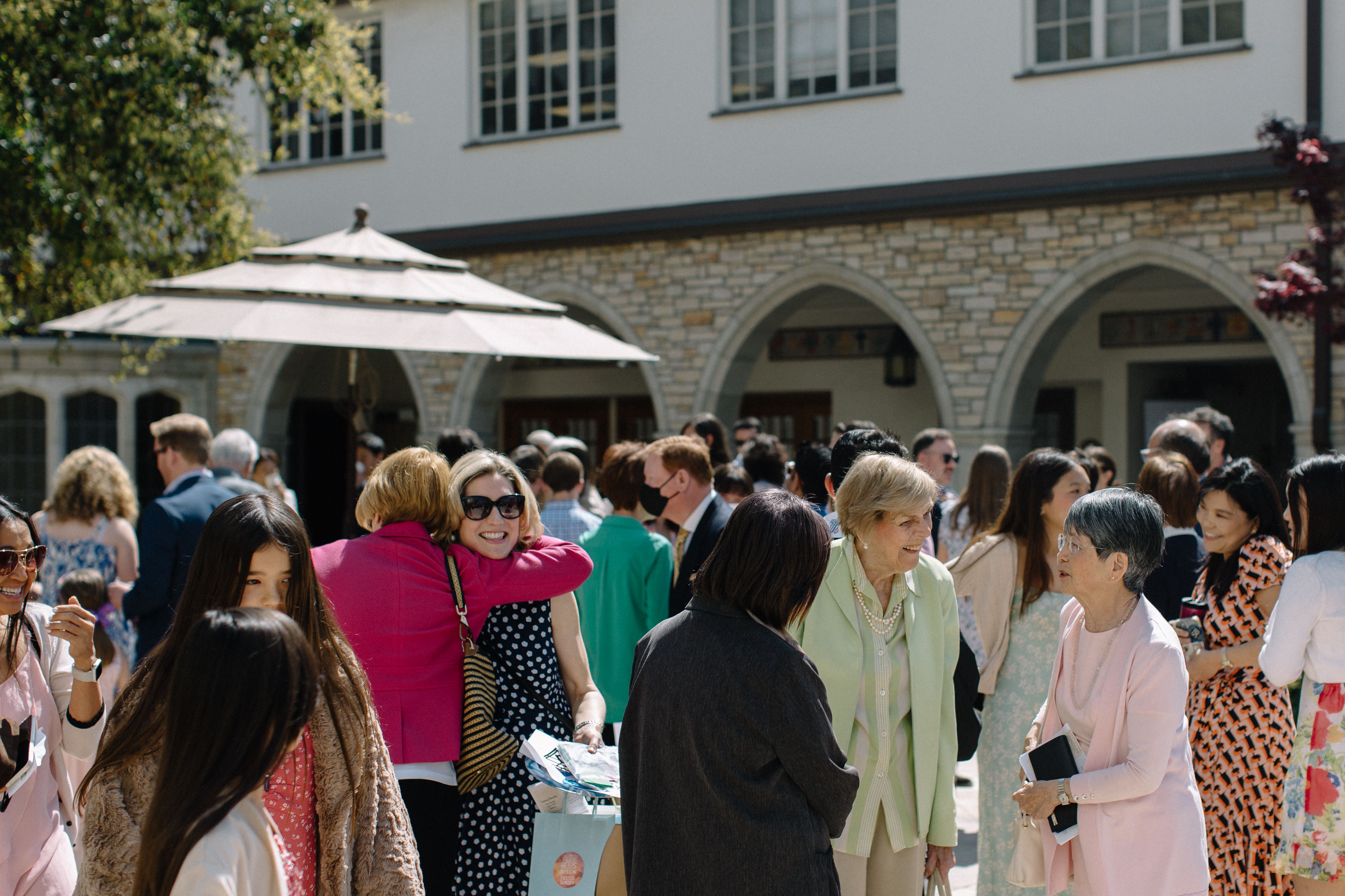 Groups of women in dresses greet one another in the courtyard at SMCC at mid-day.