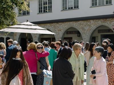 Groups of women in dresses greet one another in the courtyard at SMCC at mid-day.