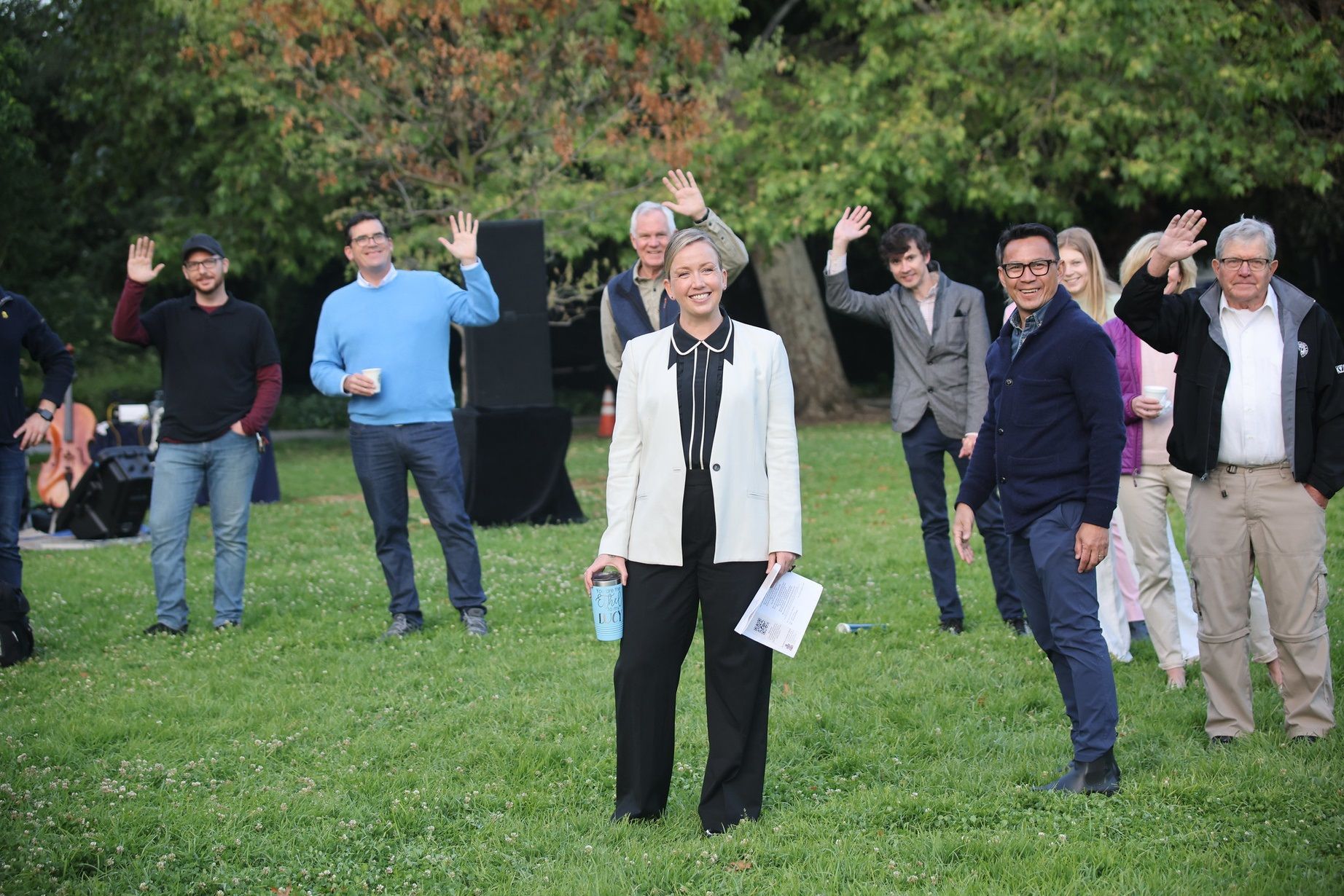 Pastoral staff and church members stand (socially distanced) in a park and wave to the camera.