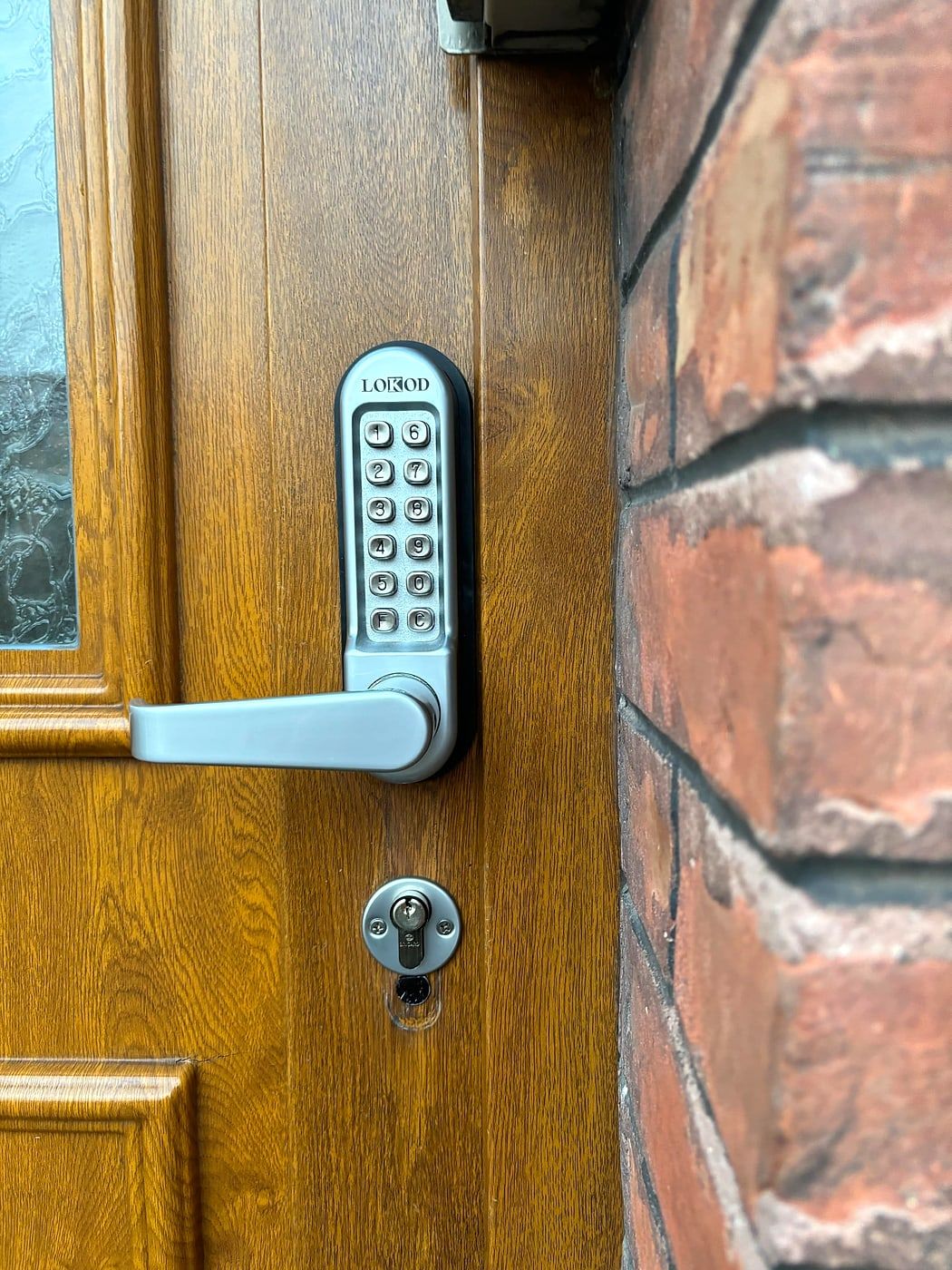 Keypad lock on a wooden door, against a brick wall