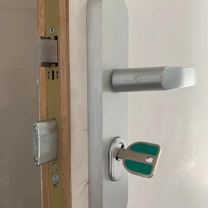 Aluminium handle and key on a white door, open edge visible