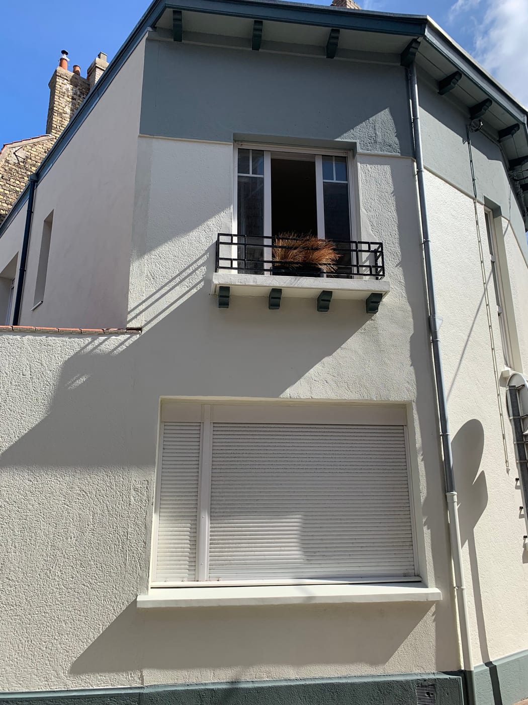 Pale facade with a closed white roller shutter on the ground floor
