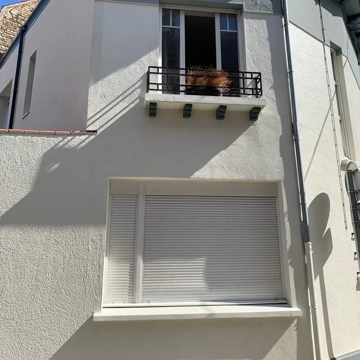 Pale facade with a closed white roller shutter on the ground floor