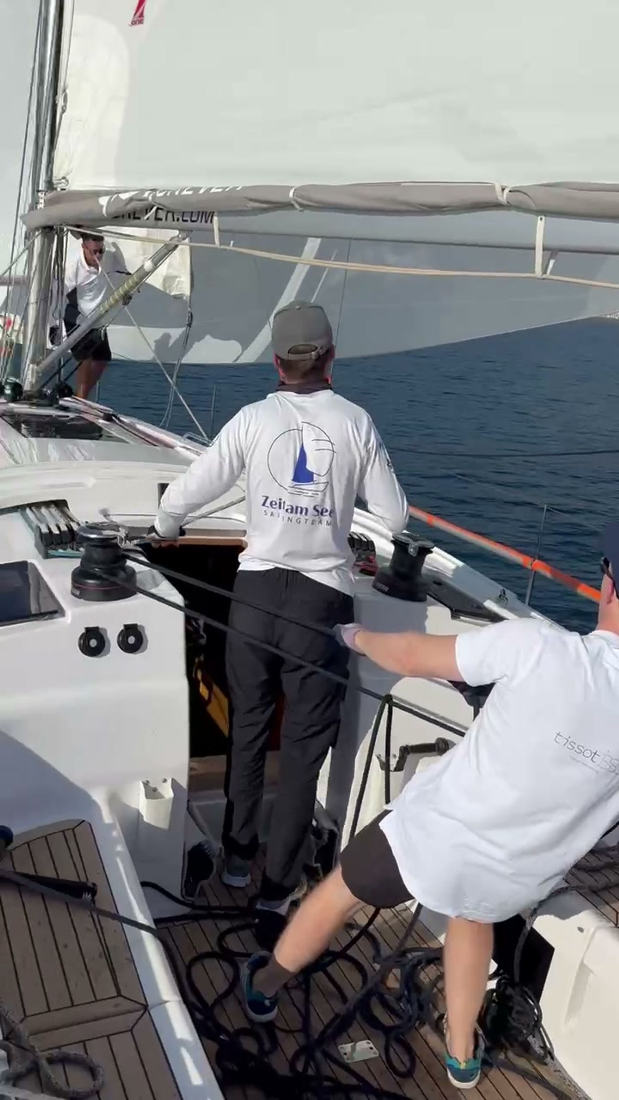 Zwei Crewmitglieder am Cockpit der Yacht, auf dem Rücken das Zeichen des Teams, tiefblaue Adria