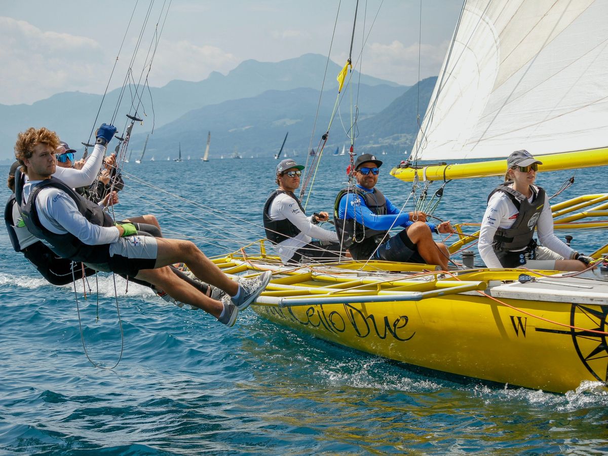 The crew of Mr. Cello Due hiking far out over the yellow hull, the Höllengebirge behind