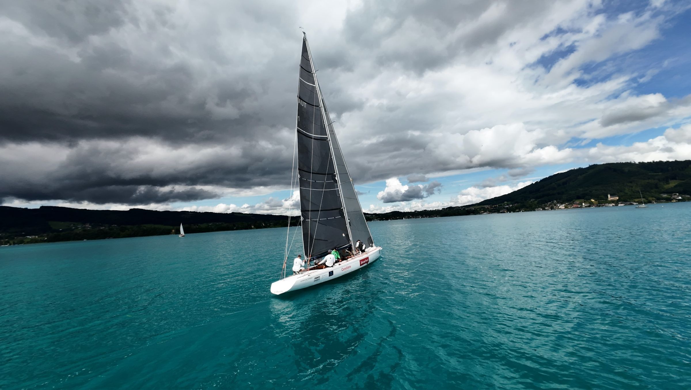 Die Liberté als kleiner Punkt auf dem Attersee unter einem breiten Wolkenband