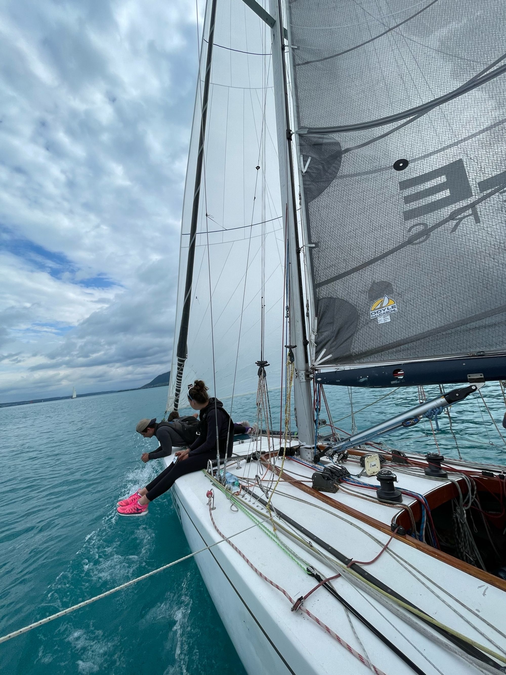 Das Boot hart am Wind, die Crew vorn an der Bordkante, darüber Vorsegel und Großsegel unter Wolken