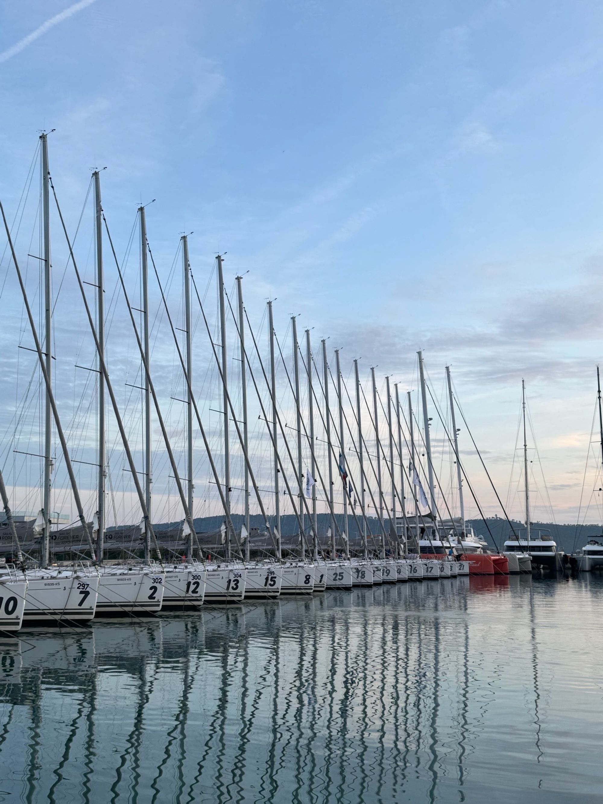 Die Einheitsflotte am Steg in Kaštela in der Morgendämmerung, die Masten spiegeln sich im Wasser