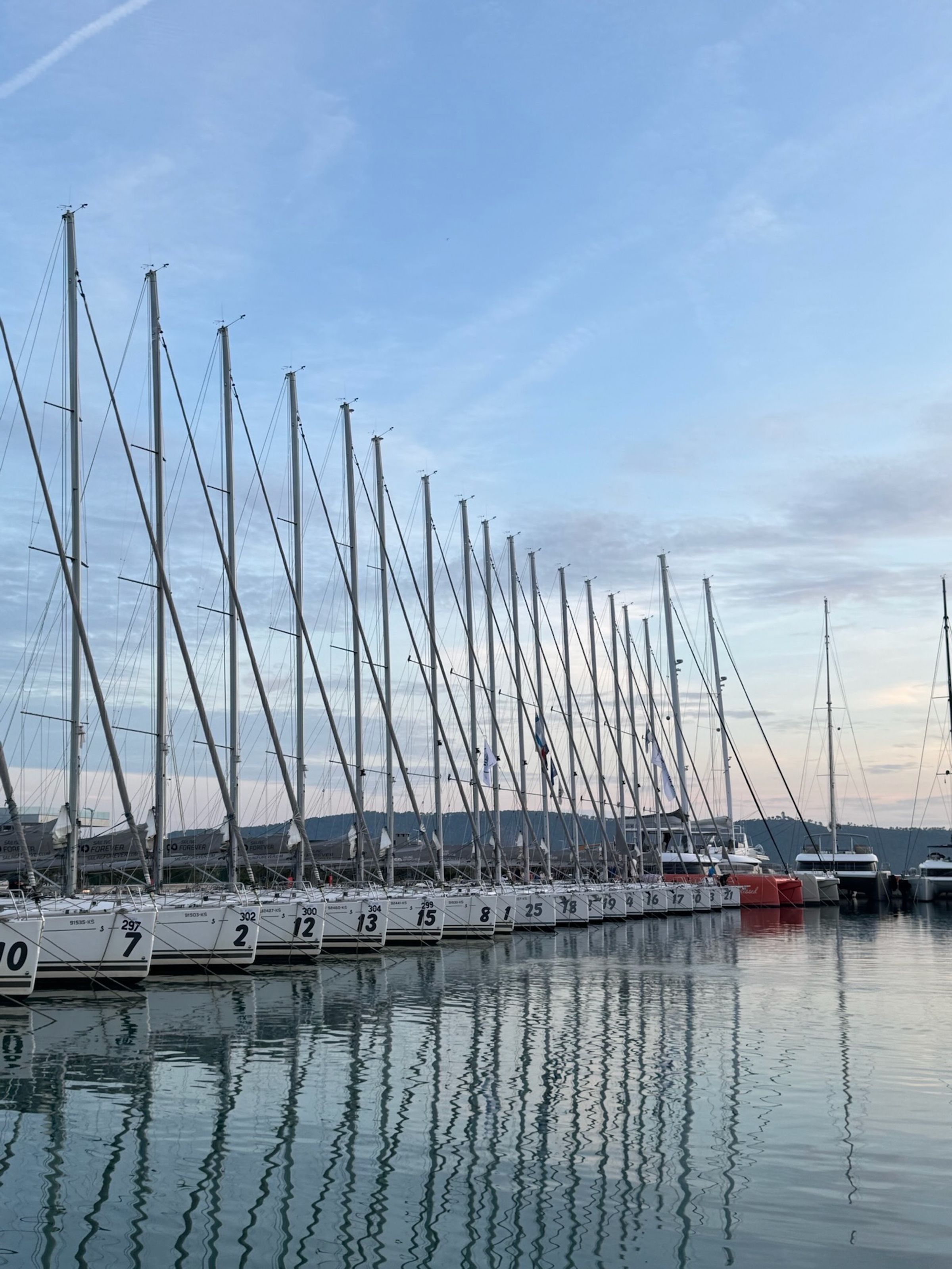 The one-design fleet at the dock in Kaštela at dawn, masts mirrored in the water