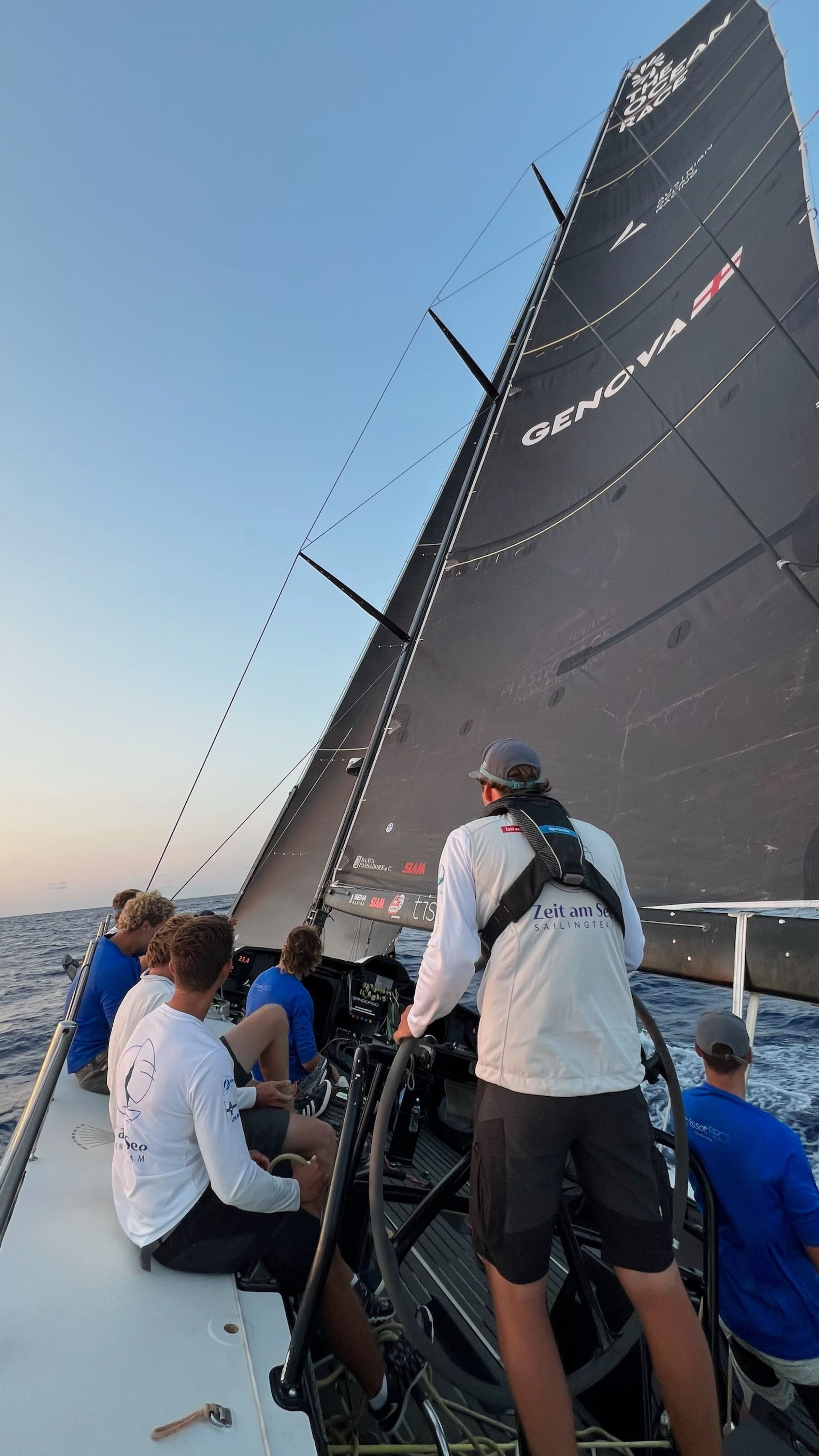 The crew on deck under genoa in evening light at sea