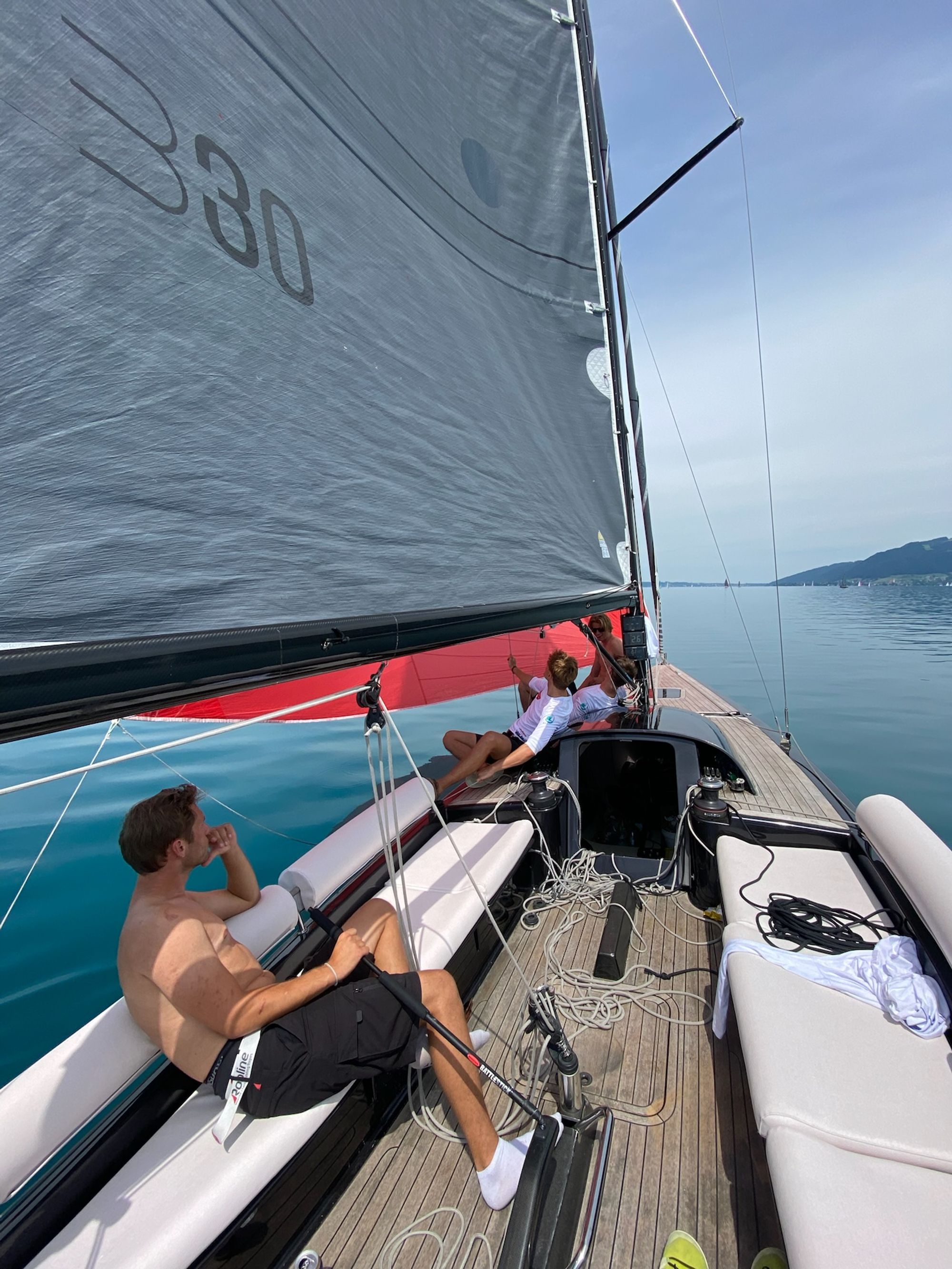 Im Großsegel das Klassenzeichen B30, vorn die Crew unter dem roten Spinnaker, glattes Wasser