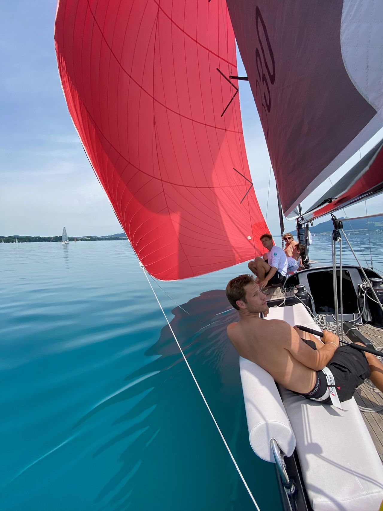 Der rote Spinnaker steht, die Crew sitzt auf der Kante über dem türkisen Wasser