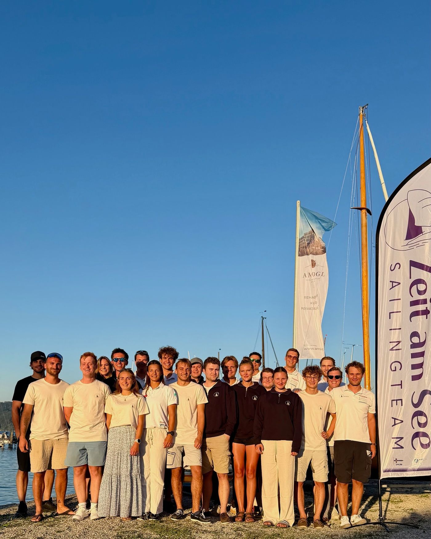 The team stands in evening light on the shore of Lake Attersee beside the club banner