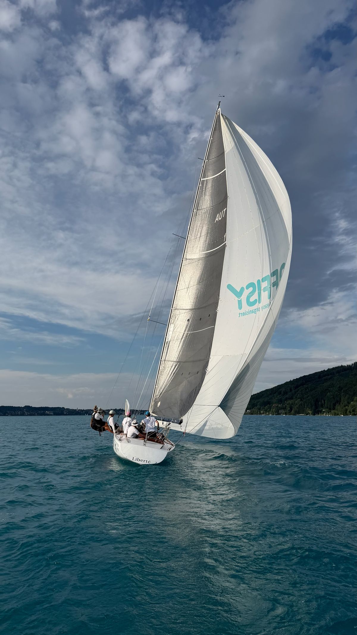 Liberté under spinnaker carrying sponsor offisy’s logo, seen from astern