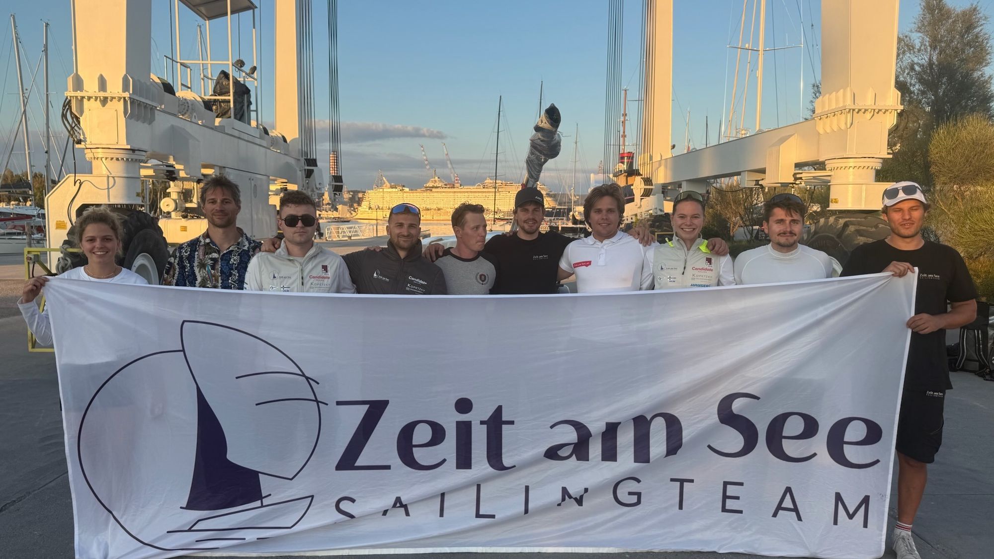 Mannschaftsbild an Land in Triest mit dem Banner des Zeit am See Sailing Teams
