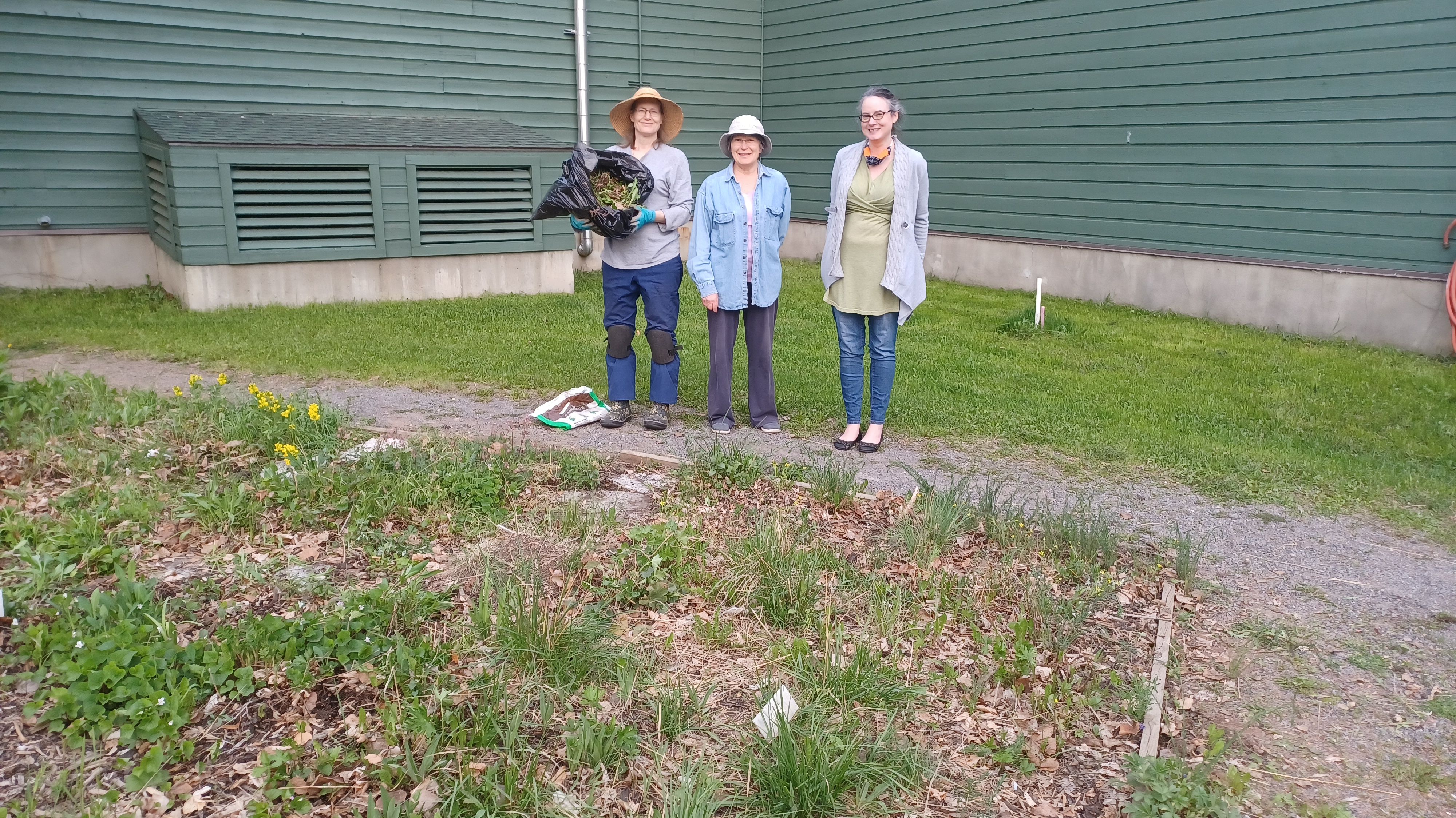 image of volunteers with a bag of weeds standing behind a native plant bed