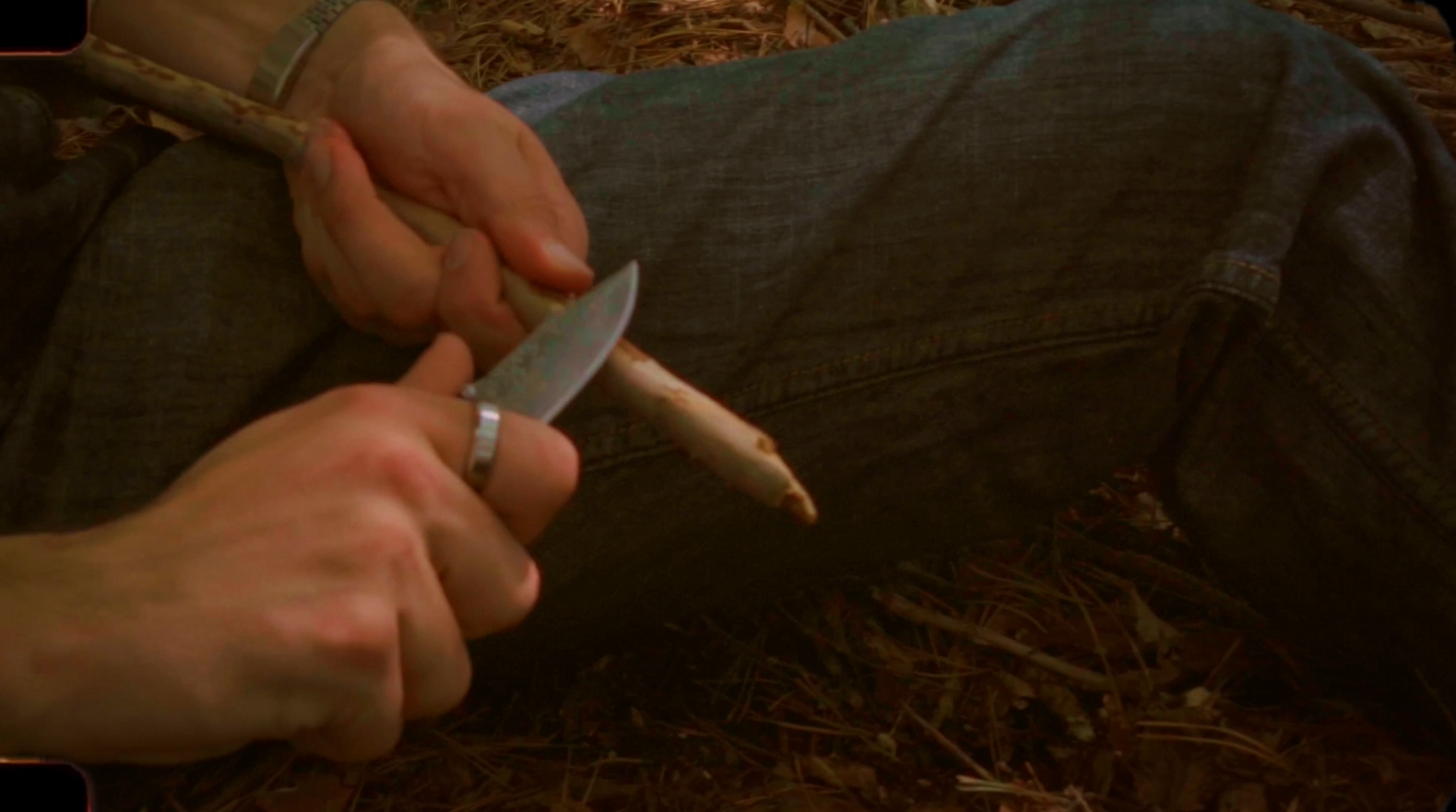 Hands carefully carve a wooden stick with a knife.