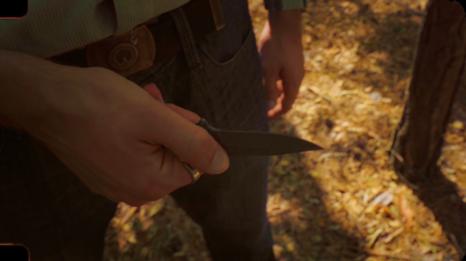 A close-up of a pocketknife held against the forest floor.