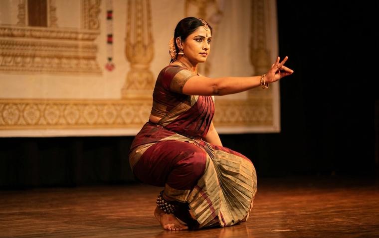 Bharatanatyam dancer in deep aramandi performing a varnam on a warm-lit stage in maroon and gold costume