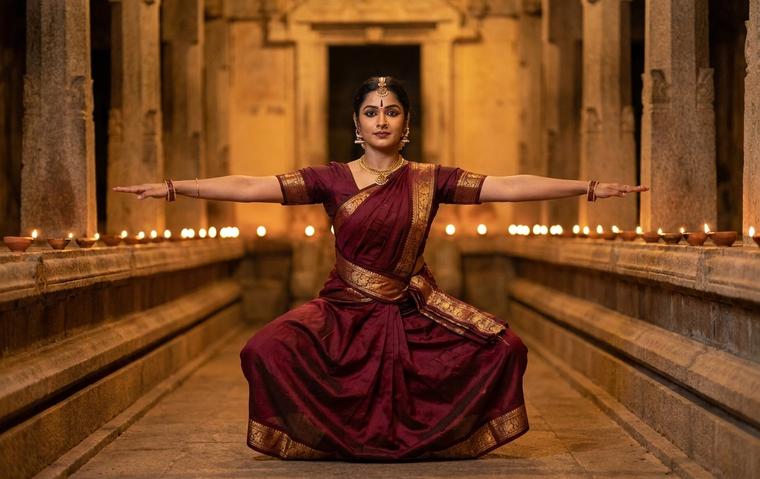 A Bharatanatyam dancer in a deep aramandi holding a strong tandava line in a lamp lit temple hall.